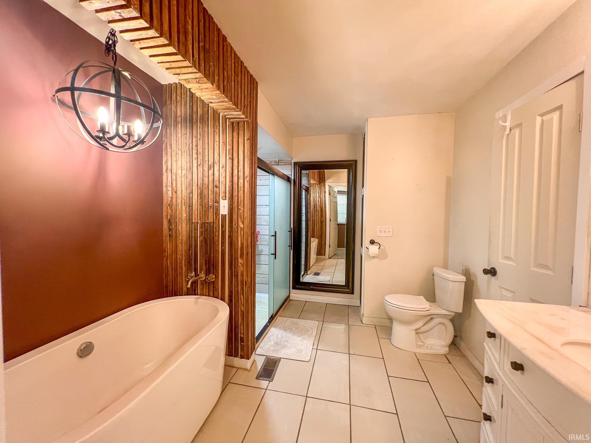 Full bathroom featuring a stall shower, vanity, a soaking tub, light tile patterned floors, and a chandelier