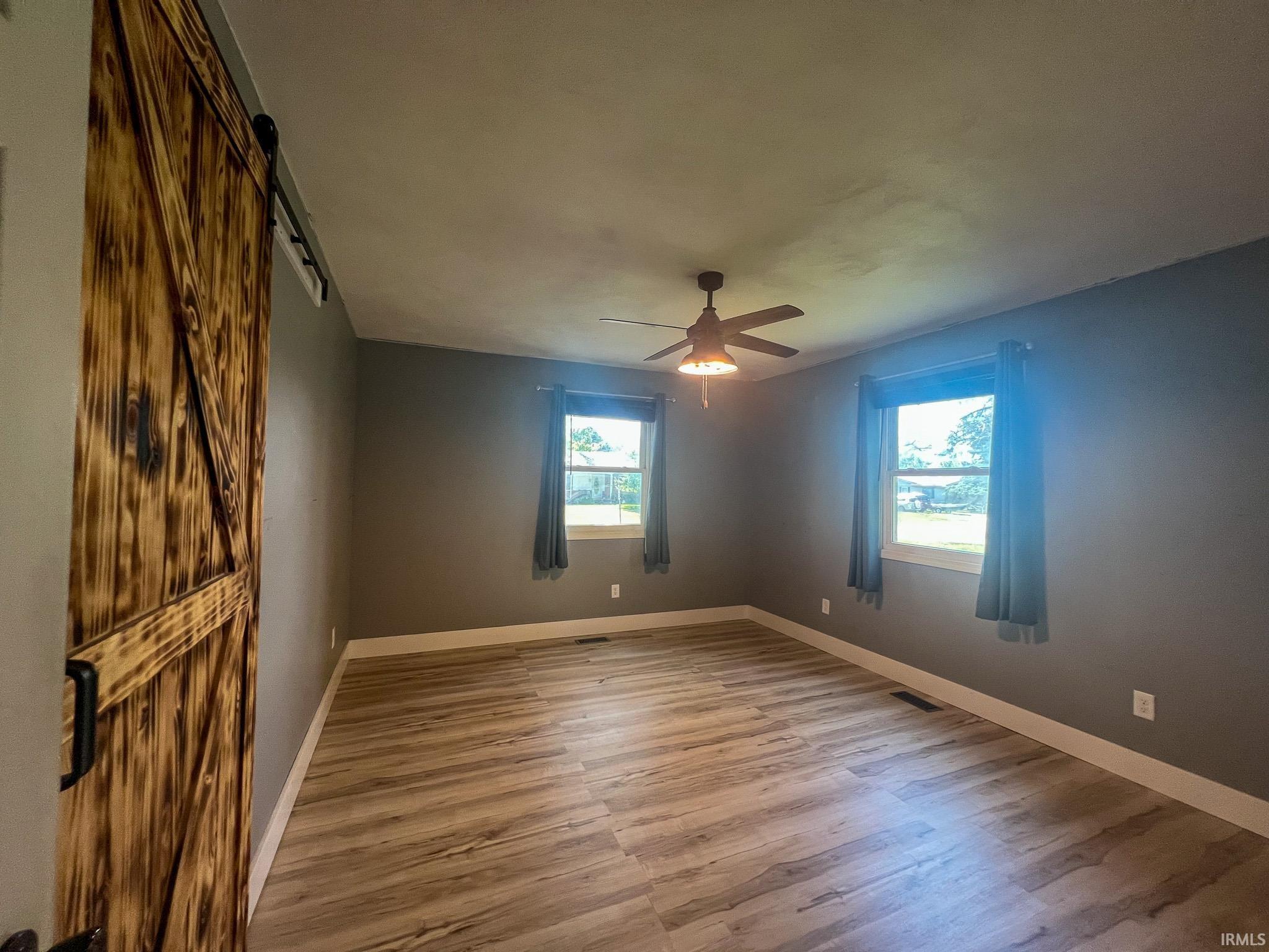 Large bedroom with a barn door, light wood finished floors, plenty of natural light, and a ceiling fan
