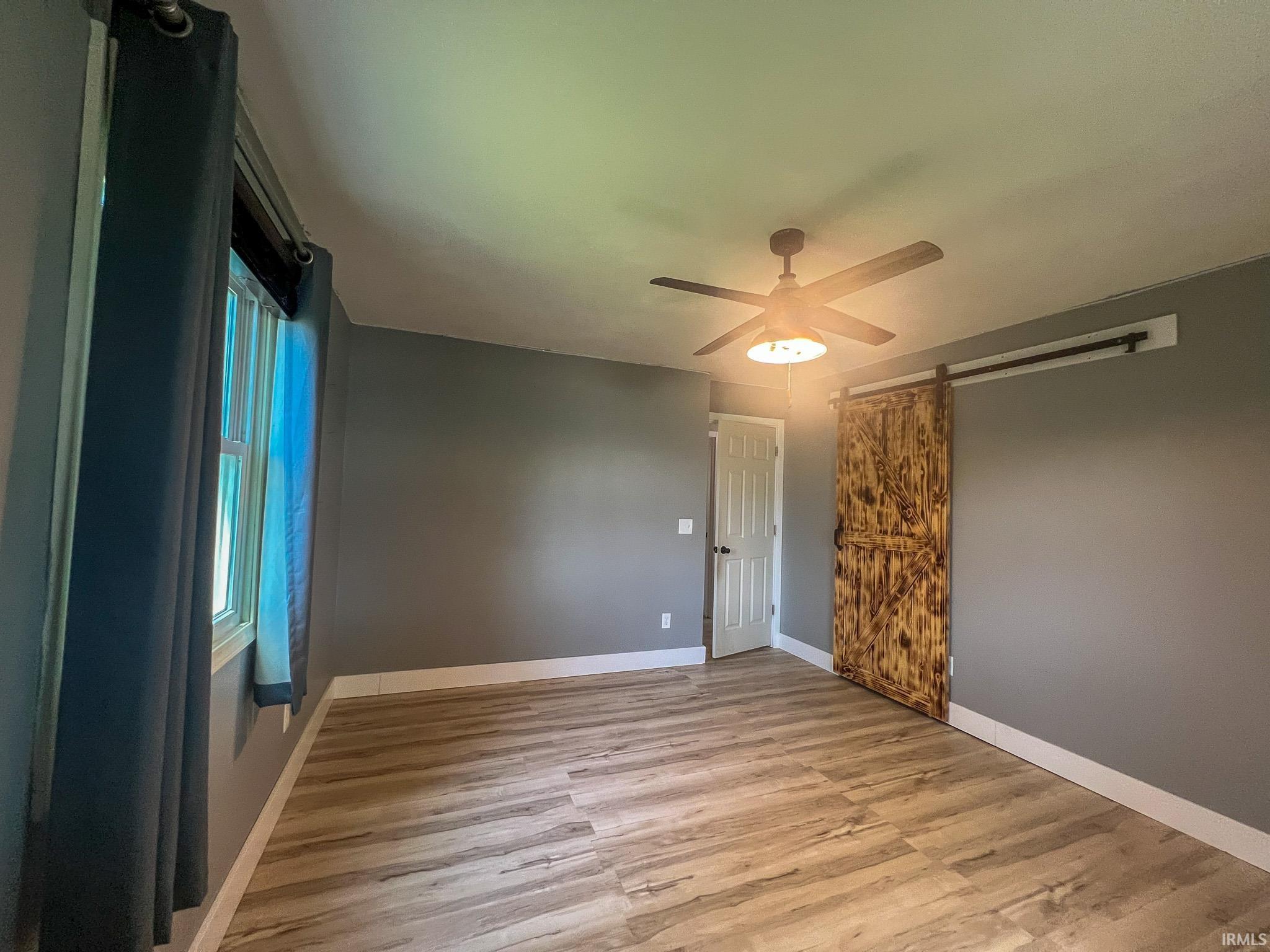 Bedroom 2 featuring a barn door, light wood-style flooring, and a ceiling fan