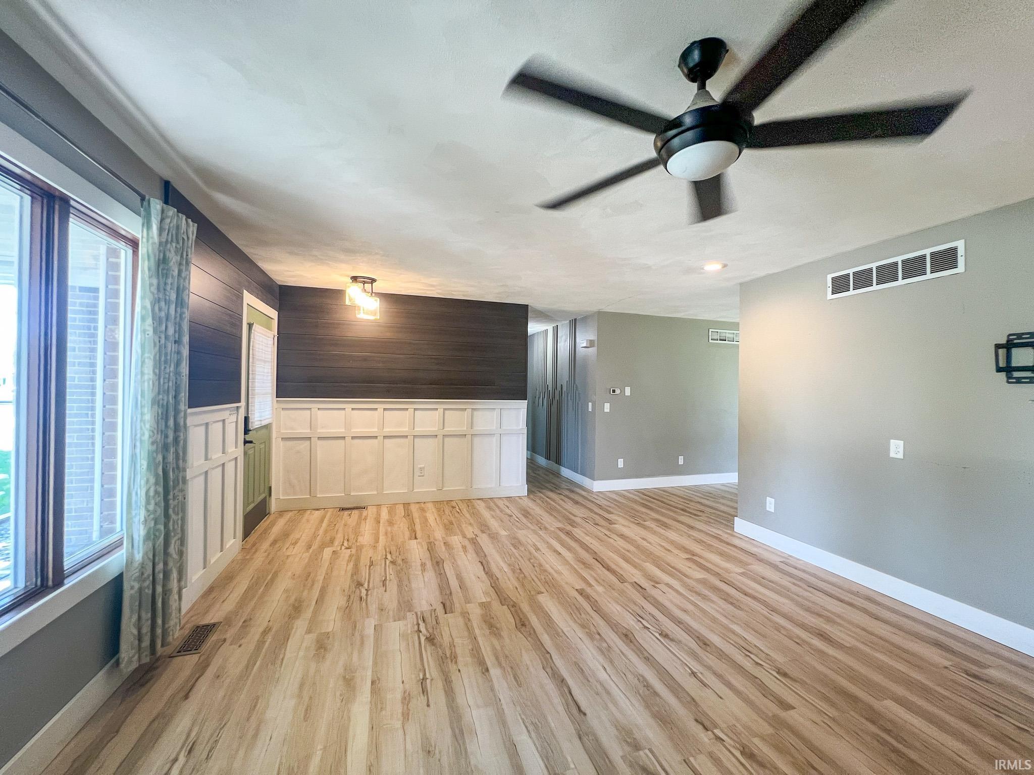 Living room featuring light wood-type flooring, ceiling fan, and a wainscoted wall