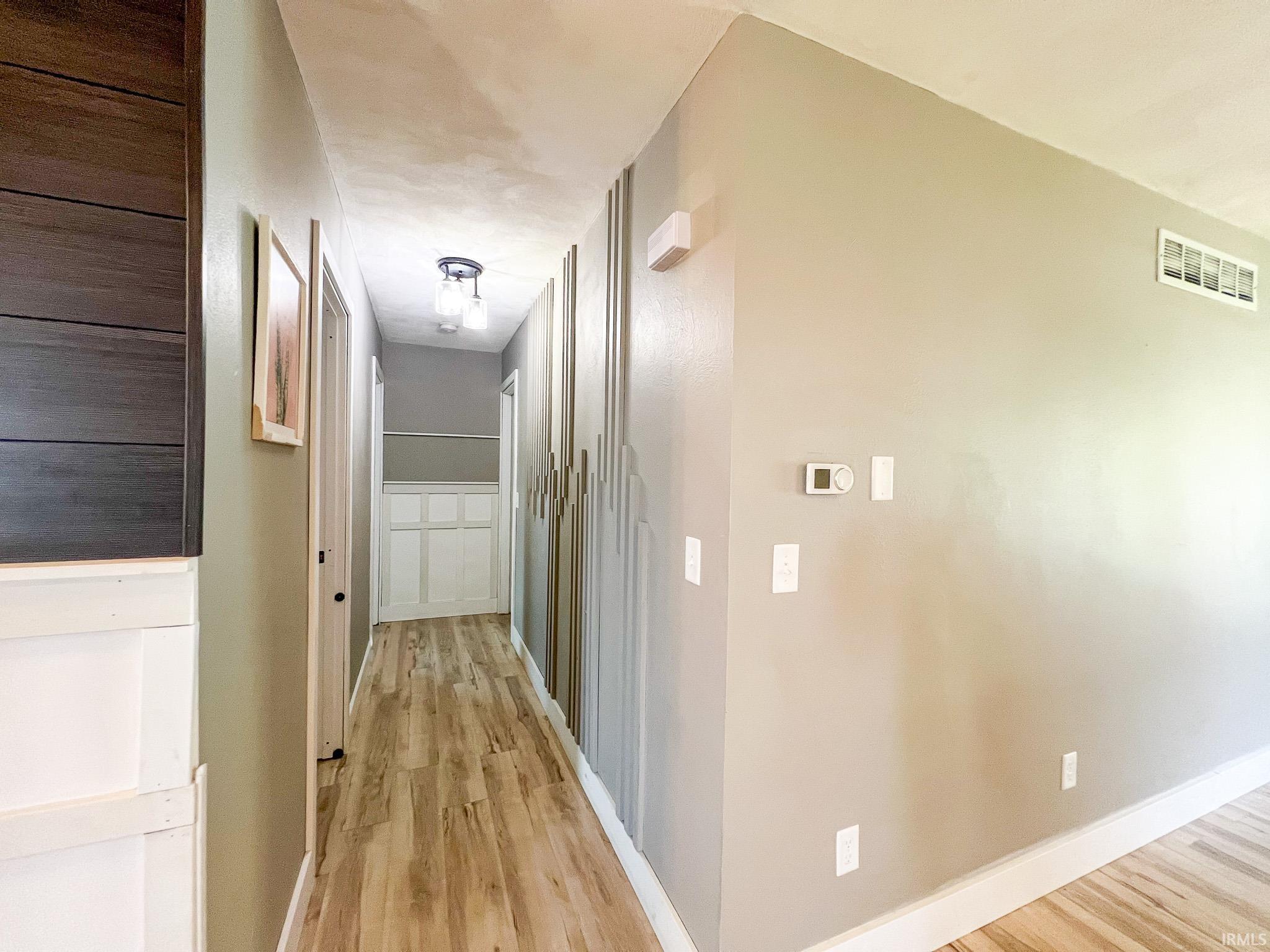 Hallway featuring light wood-style flooring and wood accented wall feature