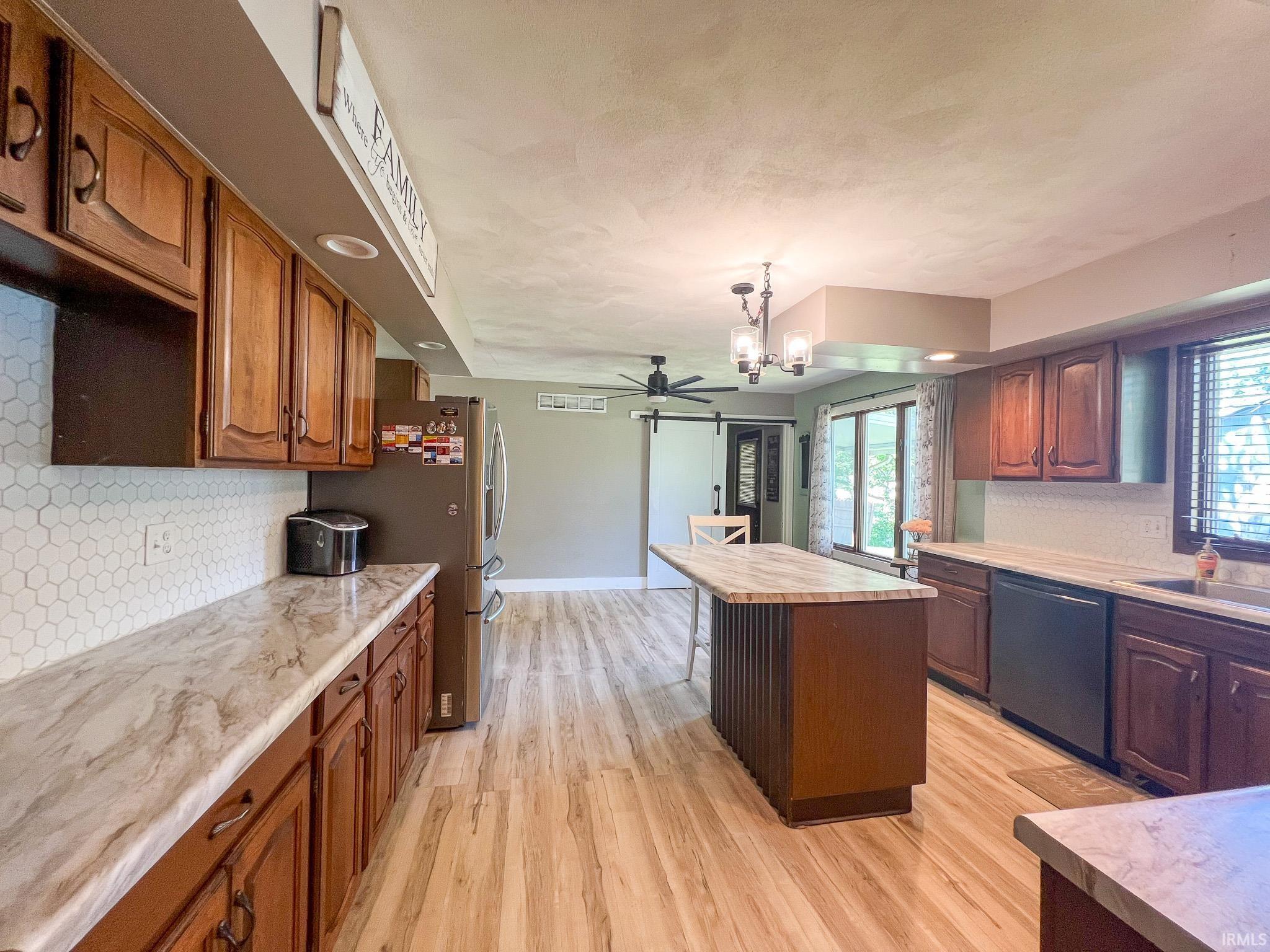 Kitchen featuring tasteful backsplash, light countertops, a kitchen island, light wood finished floors, and dishwashing machine