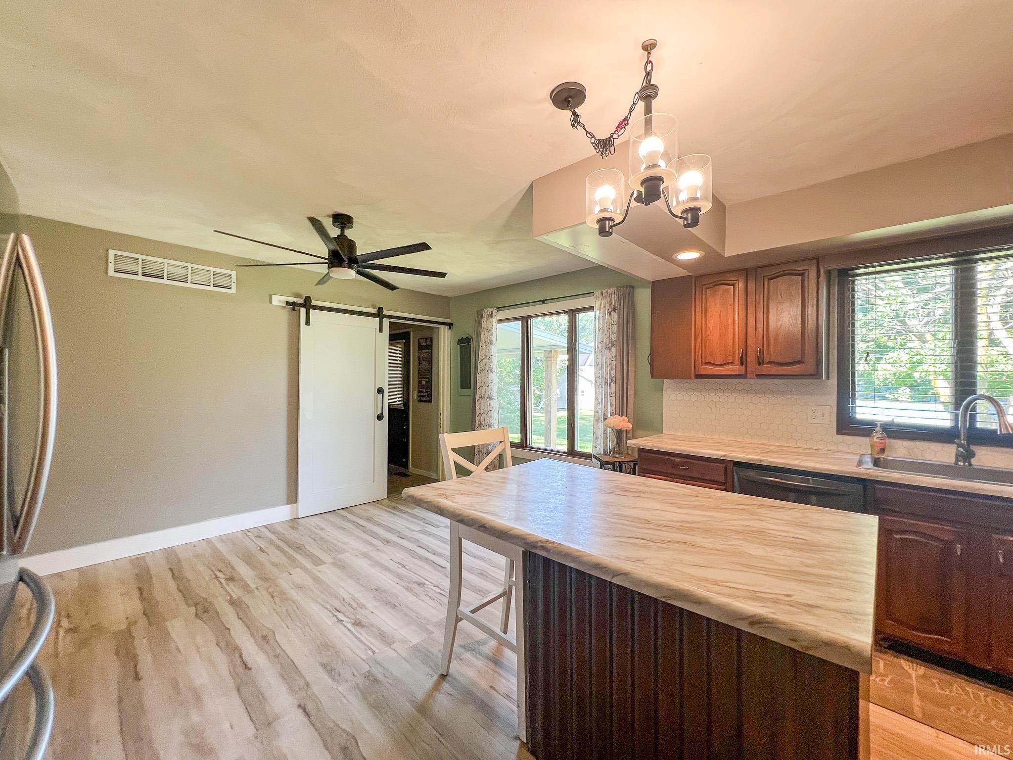 Kitchen and dining area featuring a barn door, light countertops, a kitchen island, decorative light fixtures, and light wood-style floors