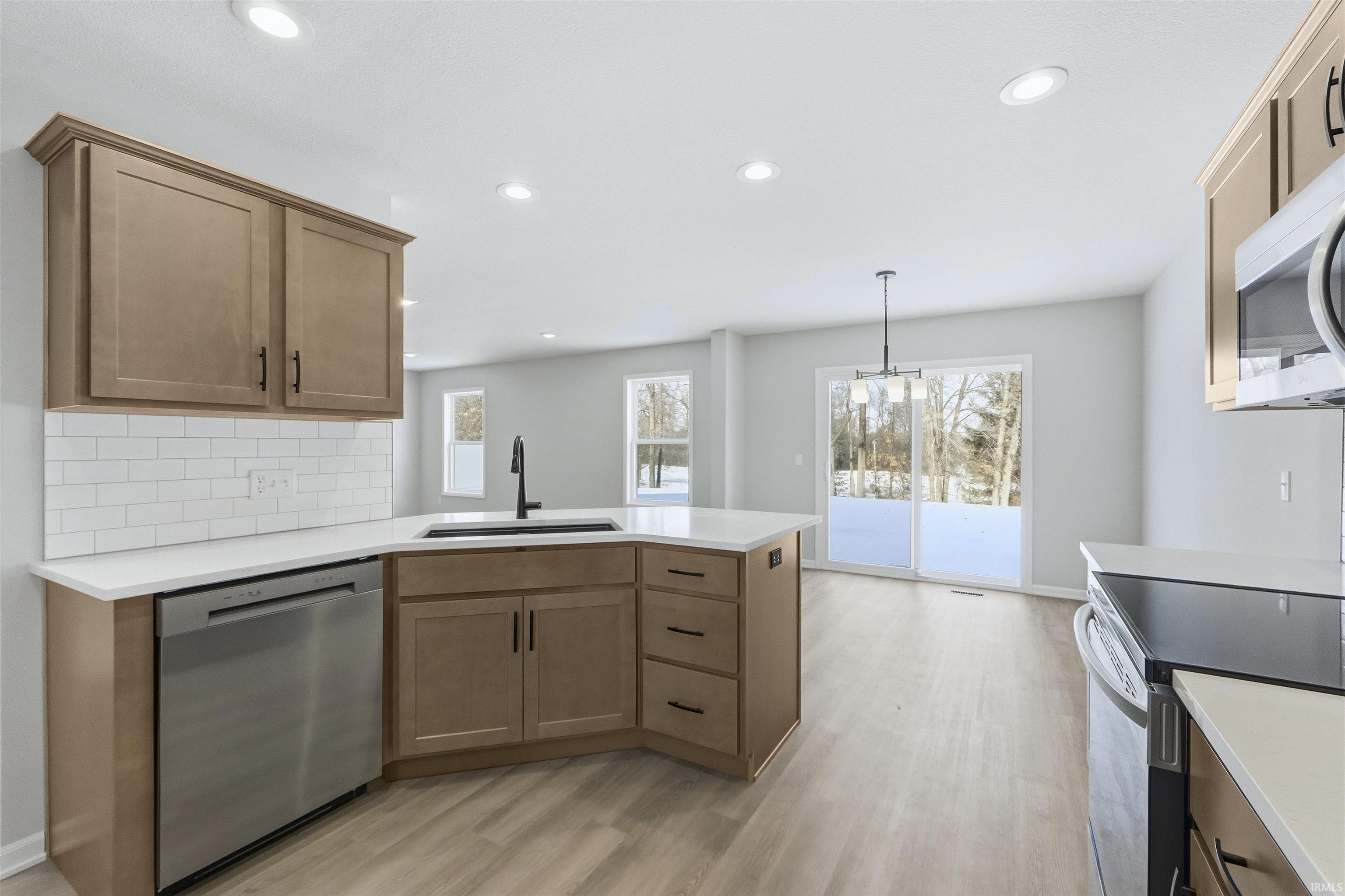 Kitchen featuring stainless steel appliances, a peninsula, backsplash, light wood-type flooring, and light stone countertops