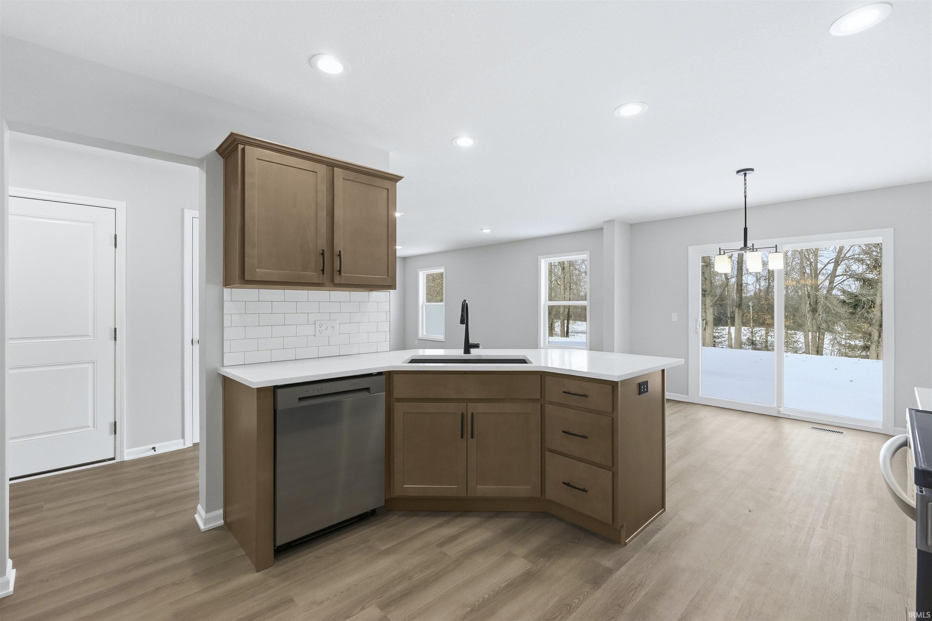 Kitchen featuring a peninsula, stainless steel dishwasher, light wood-style flooring, tasteful backsplash, and a chandelier