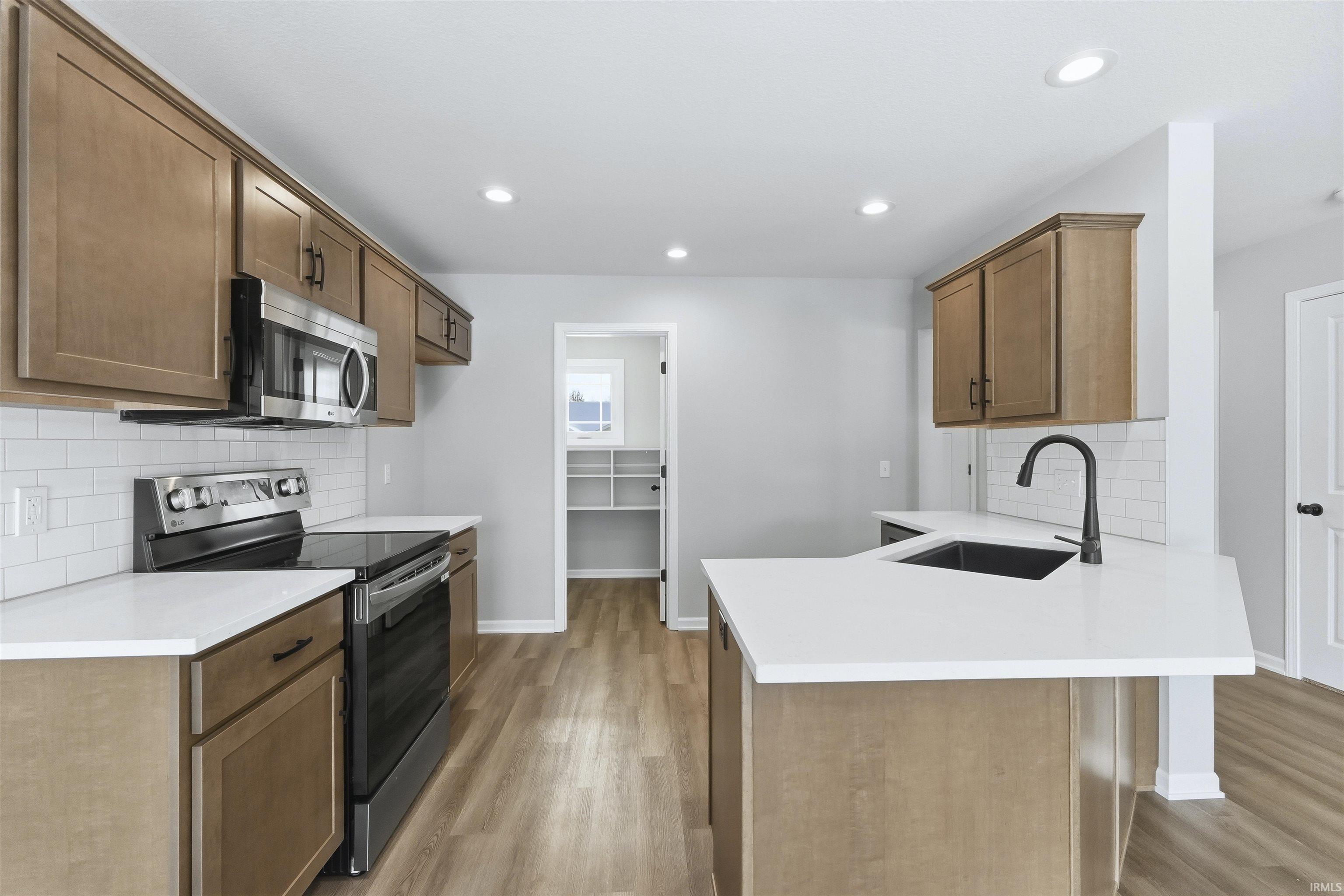 Kitchen with decorative backsplash, stainless steel appliances, a peninsula, wood finish cabinets, and light wood finished floors