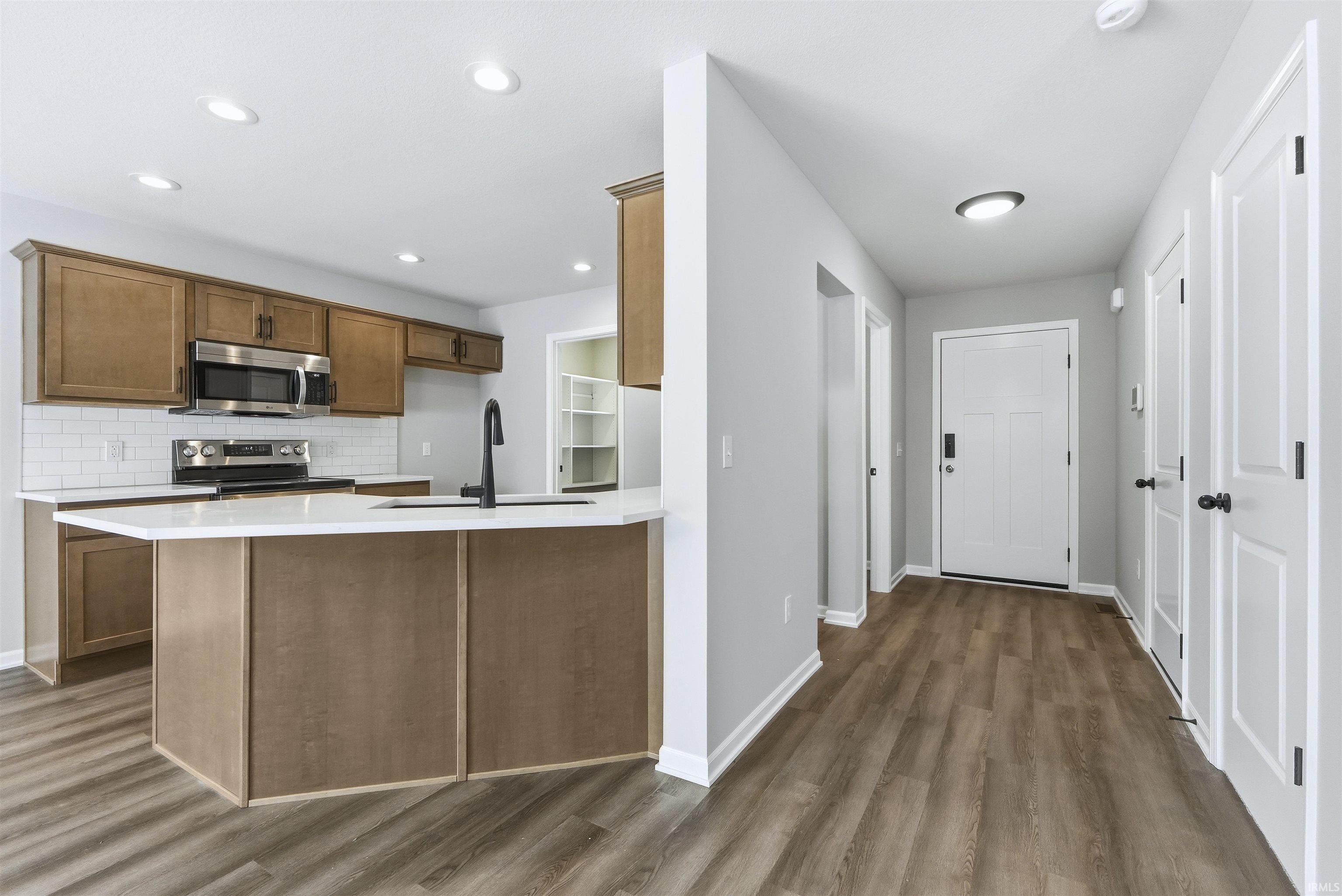 Kitchen with a peninsula, dark wood-style floors, stainless steel appliances, tasteful backsplash, and wood finish cabinetry