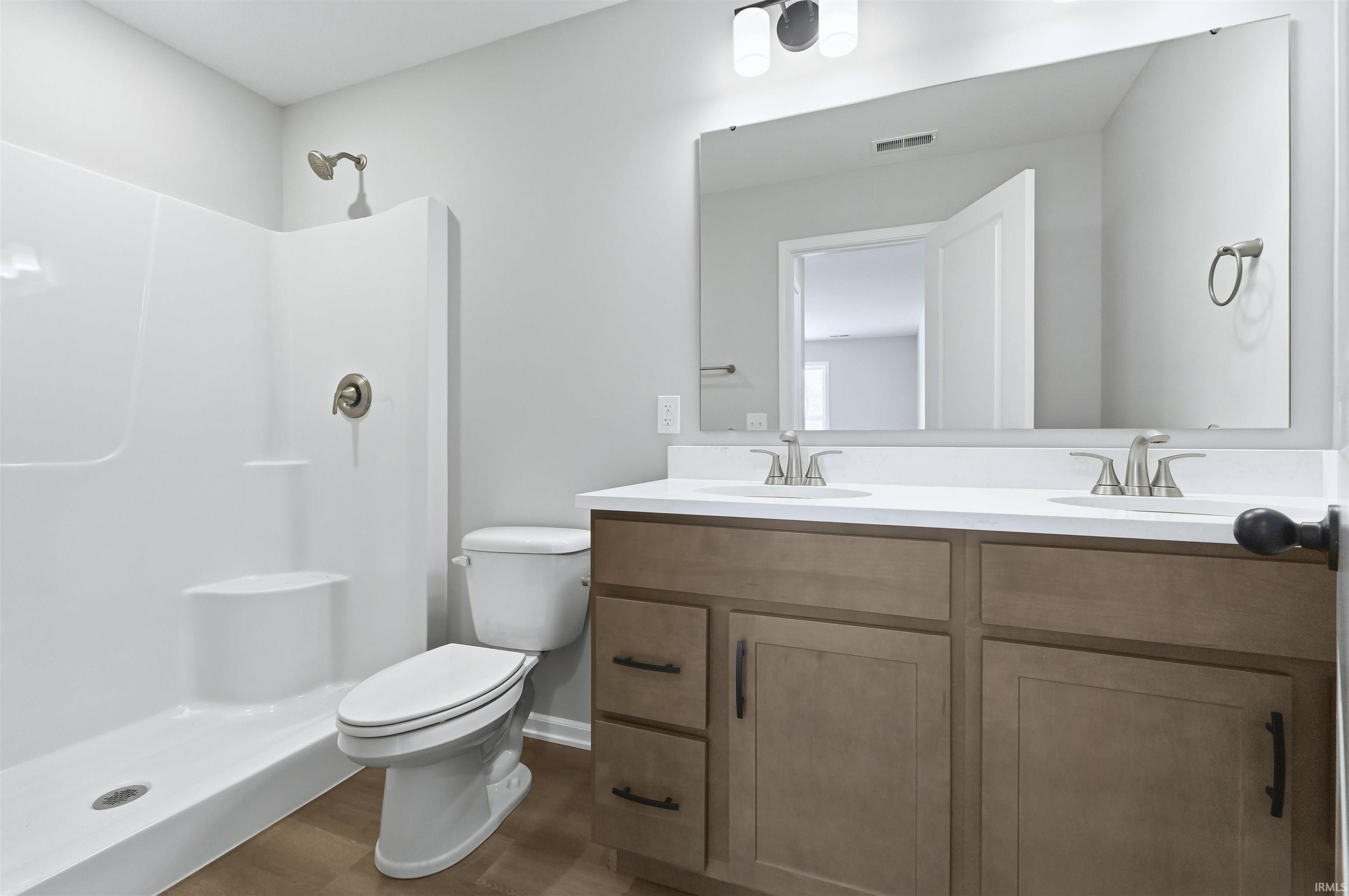 Full bath with double vanity, a shower stall, and dark wood-style flooring