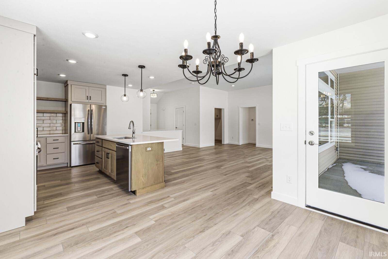 Two tone kitchen featuring a center island with sink, dual tone cabinets, stainless steel appliances, a chandelier, and open floor plan