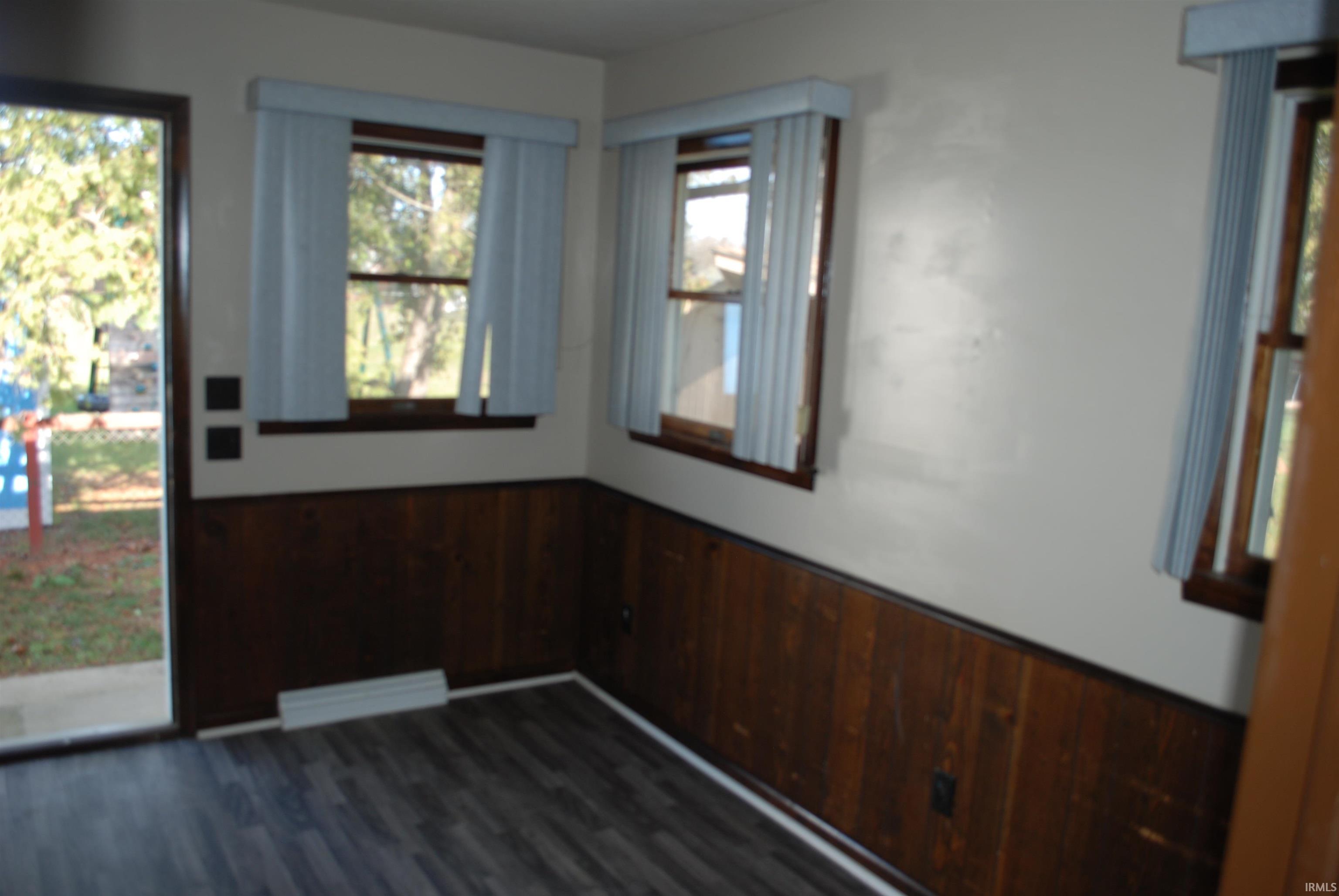 Unfurnished room featuring wood walls, wainscoting, and dark wood finished floors