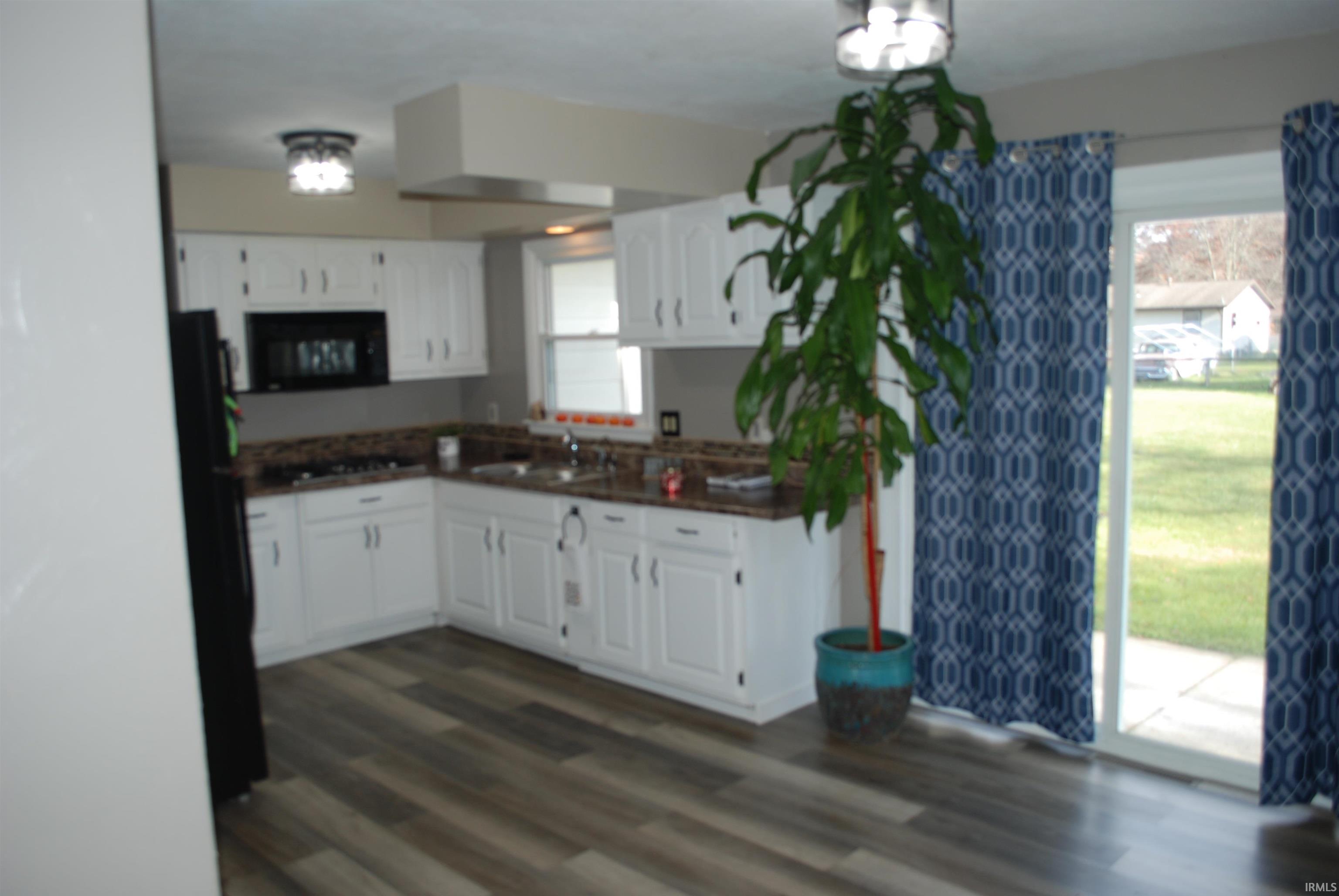 Kitchen featuring dark countertops, black appliances, dark wood-style flooring, and white cabinetry