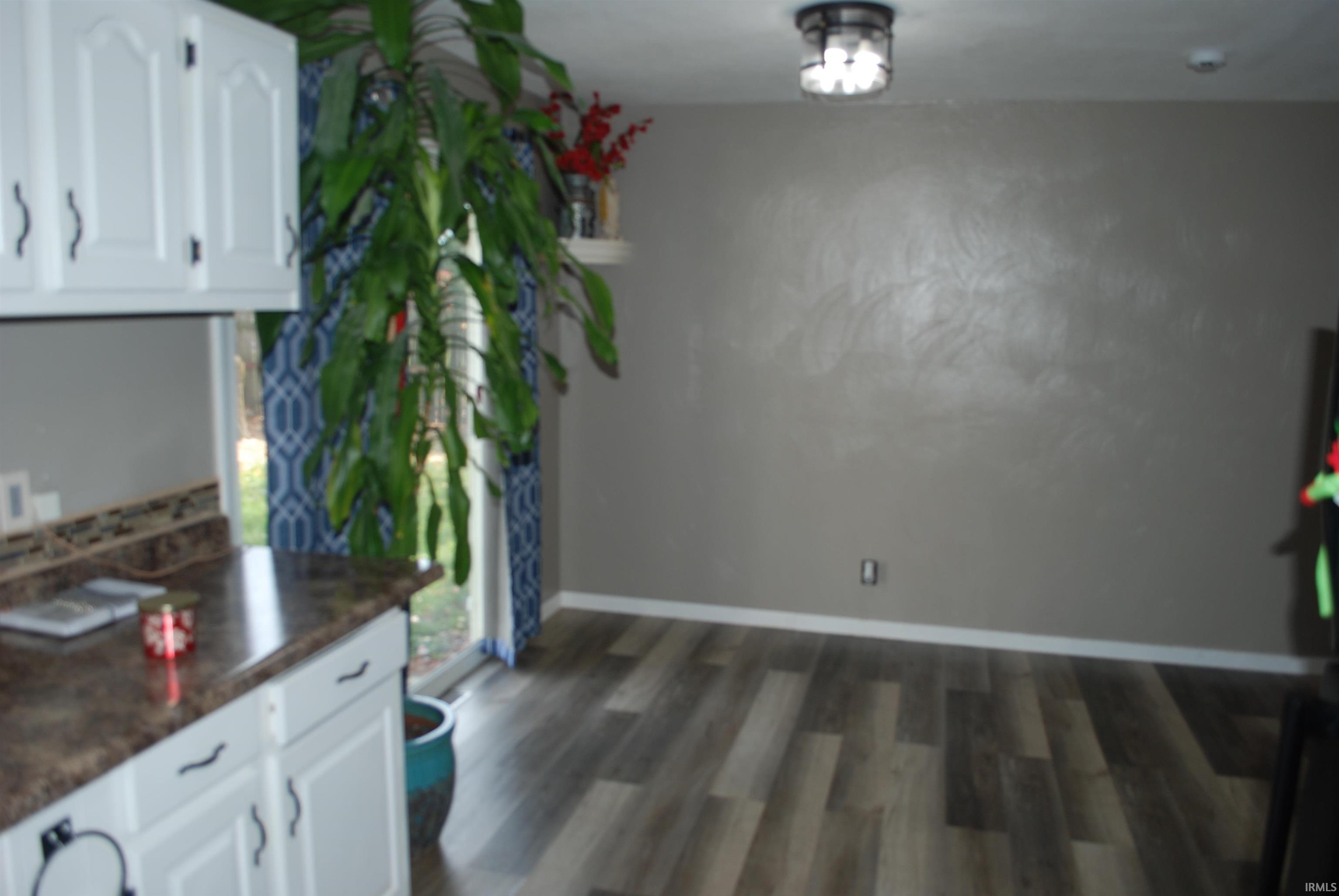 Unfurnished dining area with dark wood-style flooring and baseboards