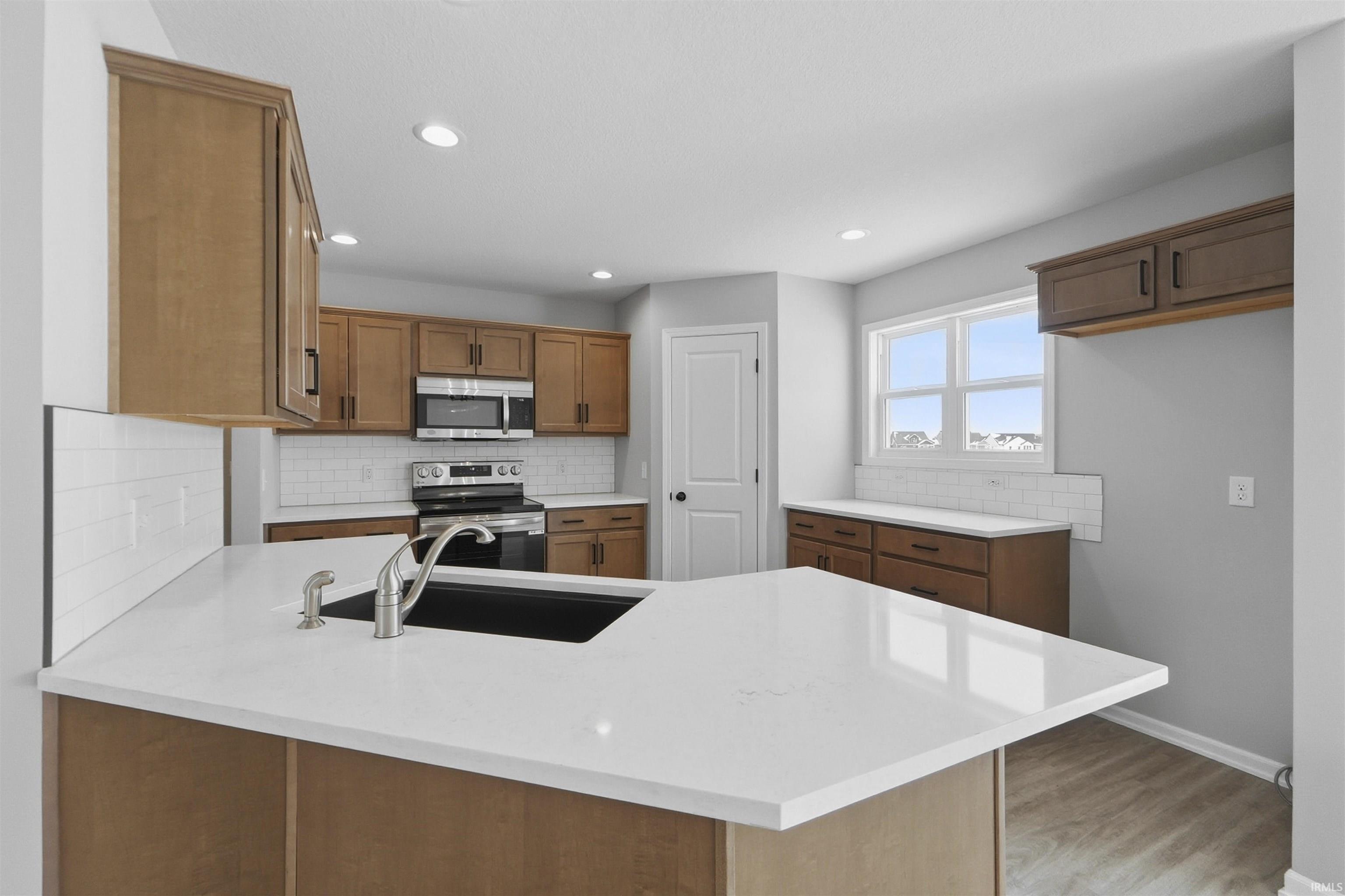 Kitchen featuring a peninsula, wood finish cabinets, stainless steel appliances, tasteful backsplash, and light wood-style flooring