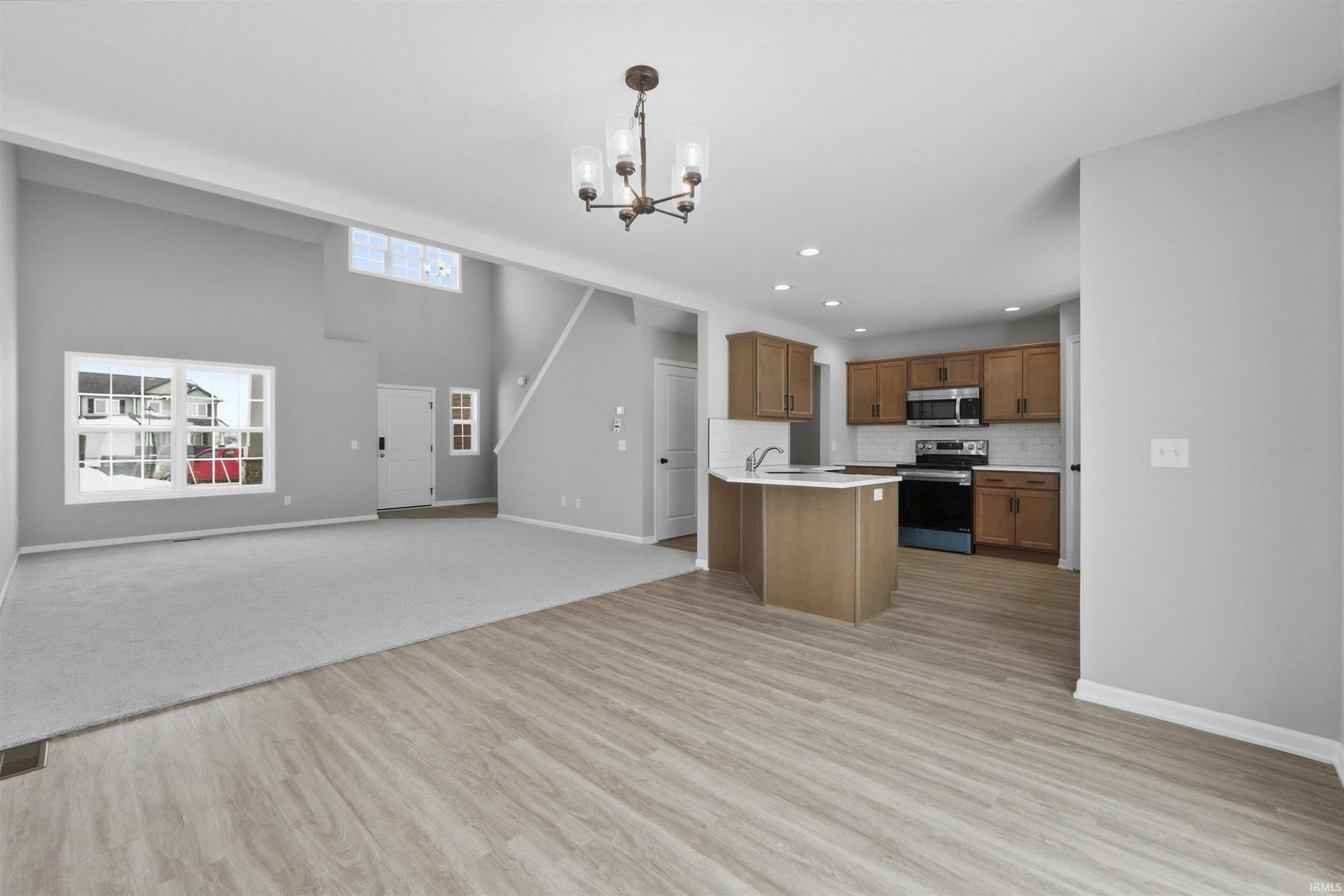 Kitchen featuring open floor plan, wood finish cabinets, light countertops, hanging lights, and stainless steel appliances