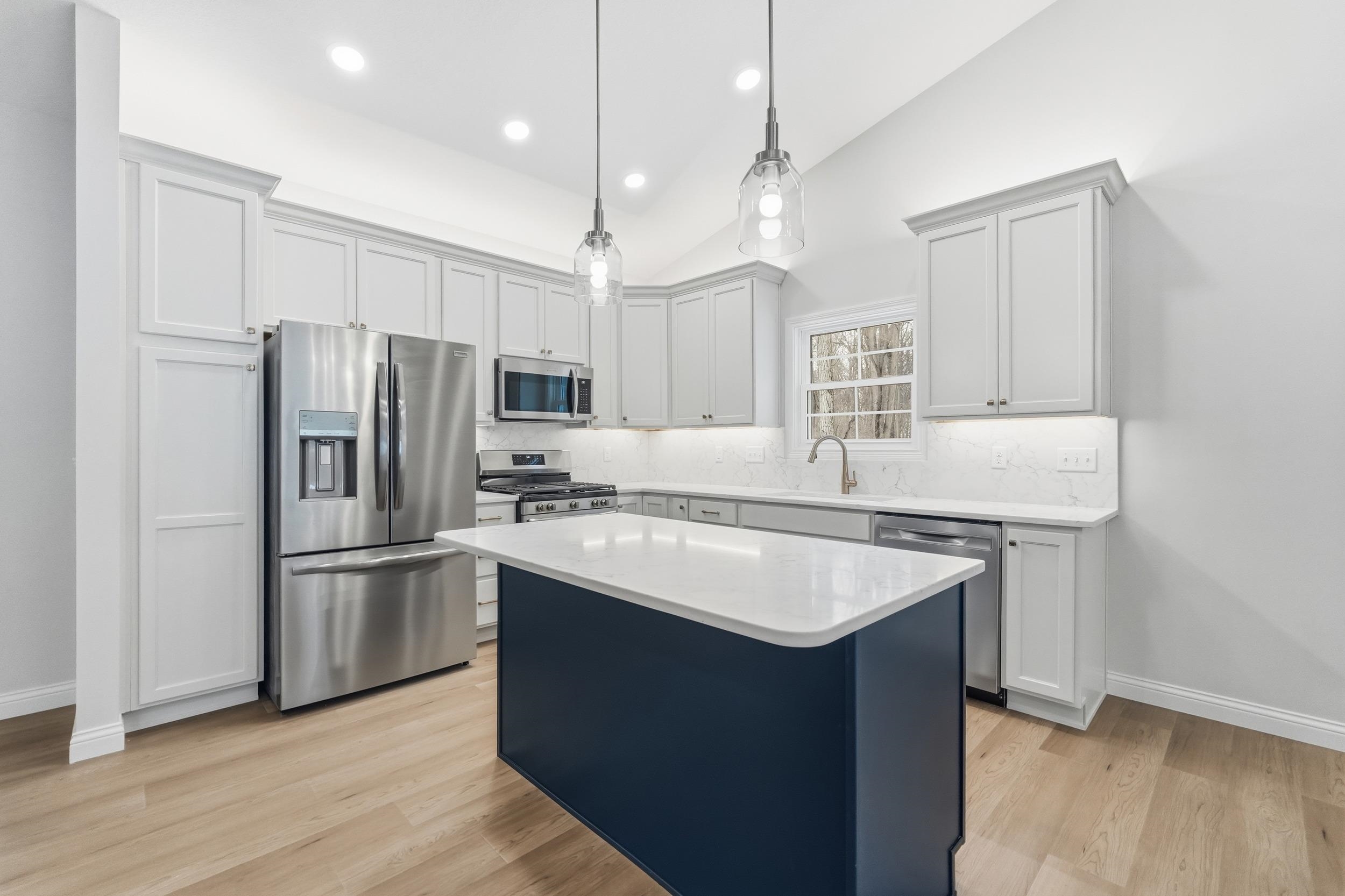 Kitchen with stainless steel appliances, vaulted ceiling, a kitchen island, light wood-type flooring, and decorative light fixtures