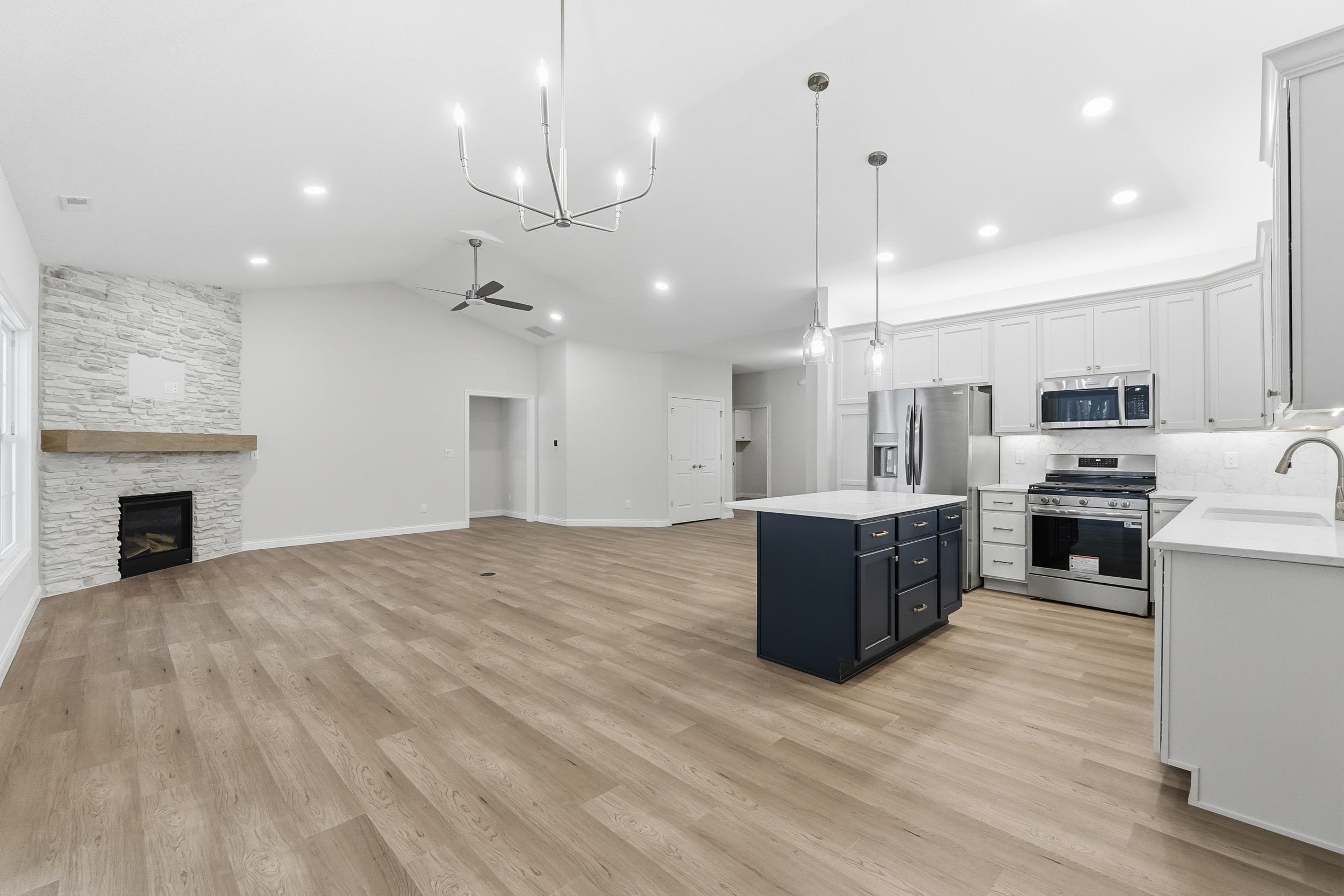 Kitchen featuring stainless steel appliances, a stone fireplace, white cabinetry, open floor plan, and a chandelier