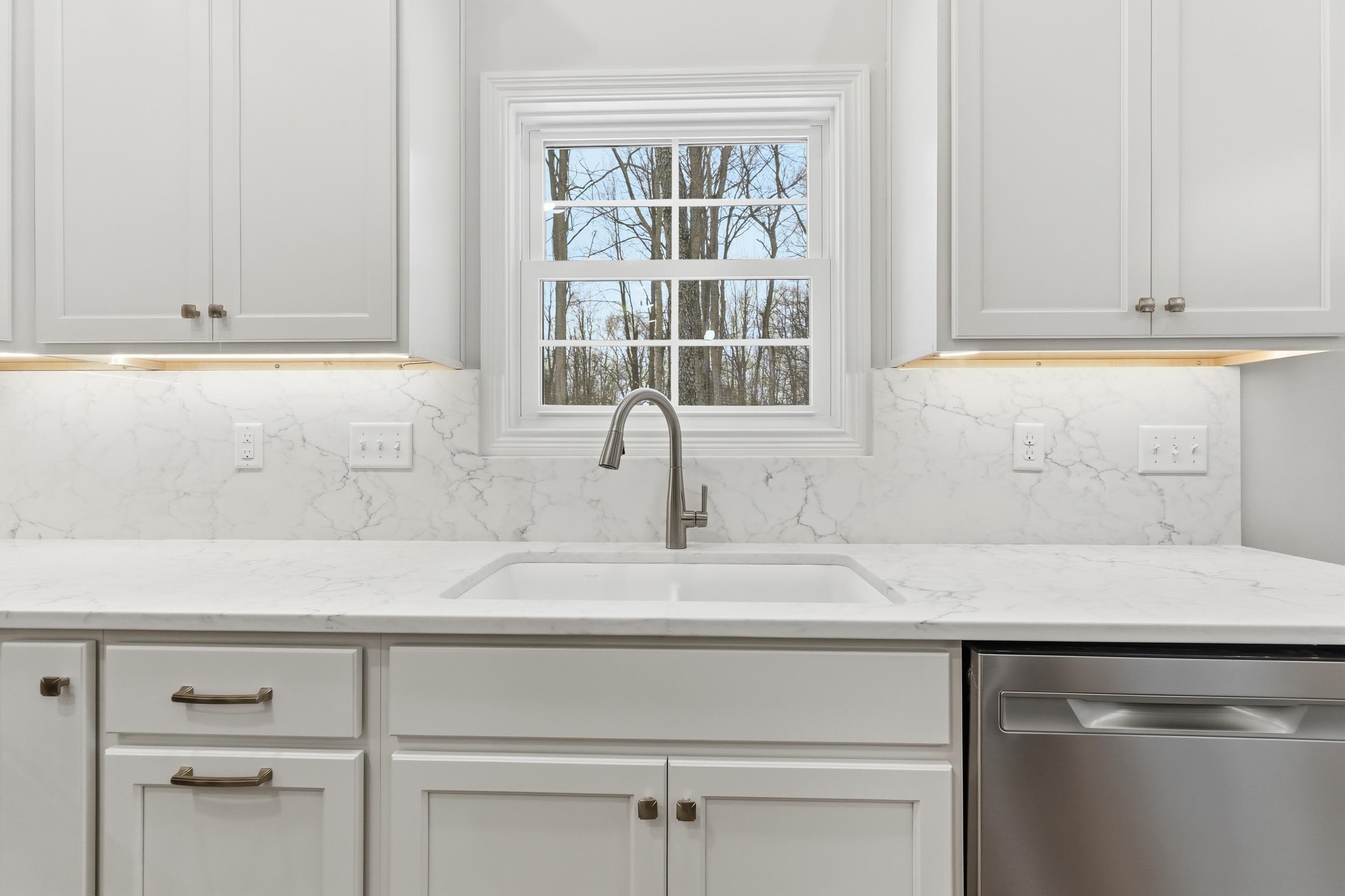 Kitchen with stainless steel dishwasher, white cabinetry, light stone counters, and backsplash
