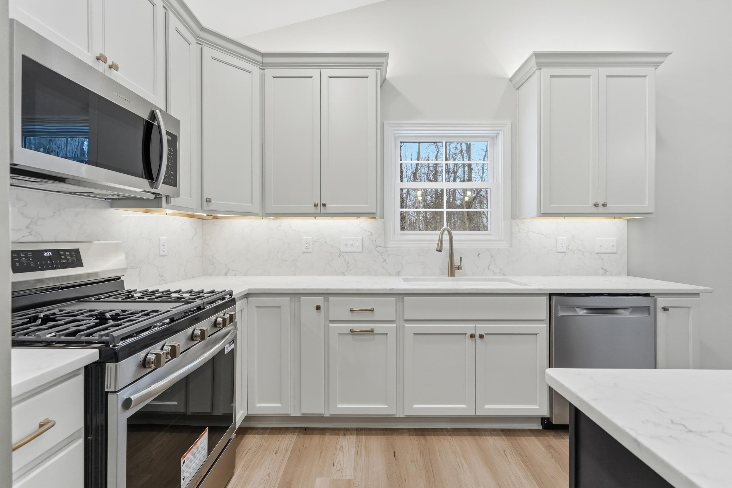 Kitchen with appliances with stainless steel finishes, white cabinets, light stone counters, light wood-style flooring, and tasteful backsplash