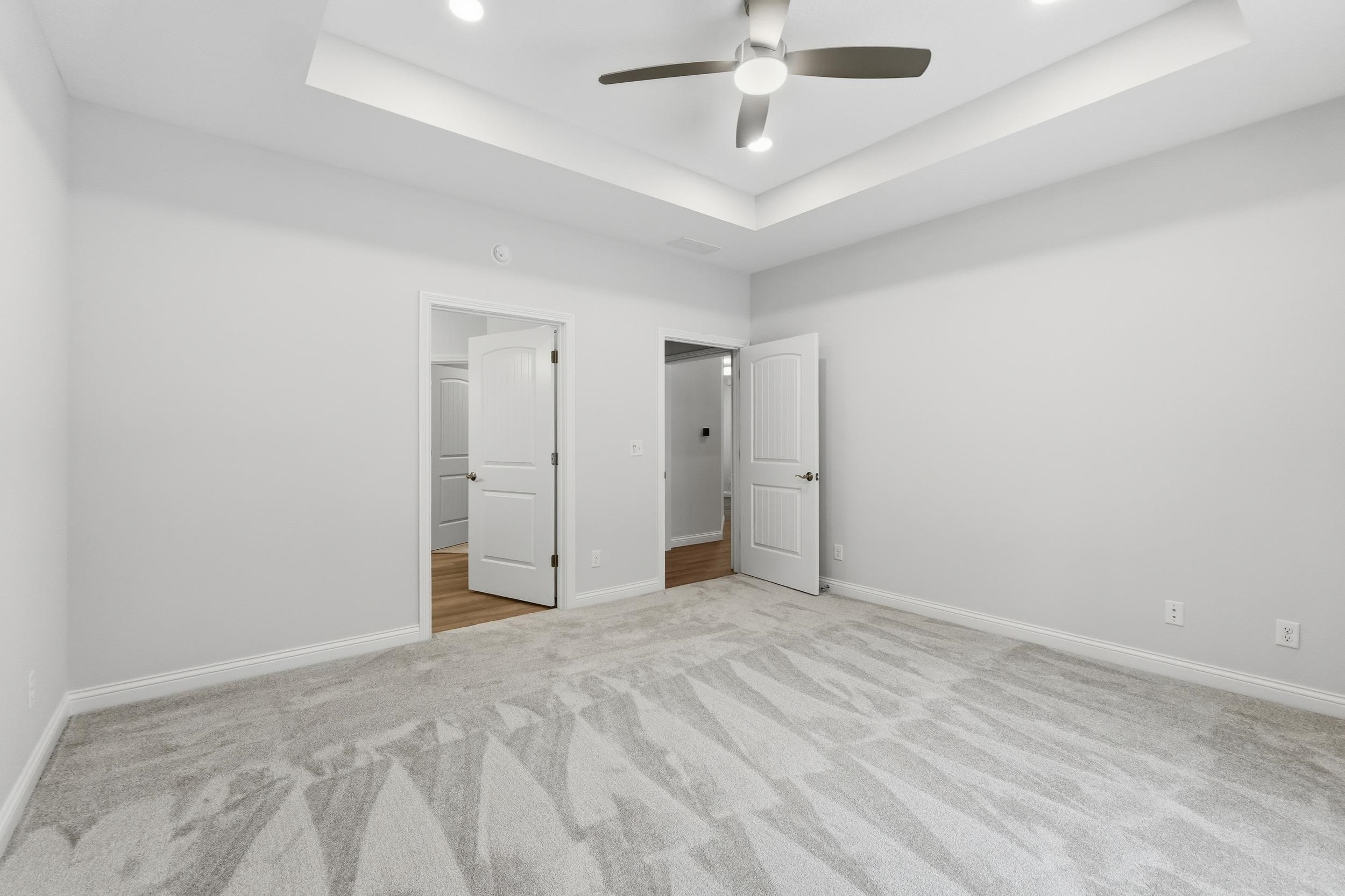Unfurnished bedroom with a raised ceiling, ceiling fan, light carpet, and recessed lighting