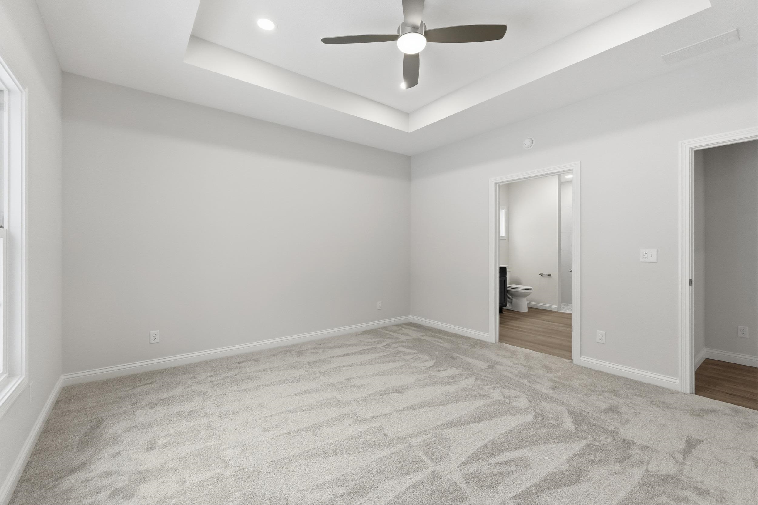 Unfurnished bedroom featuring a raised ceiling, a ceiling fan, light colored carpet, and ensuite bath