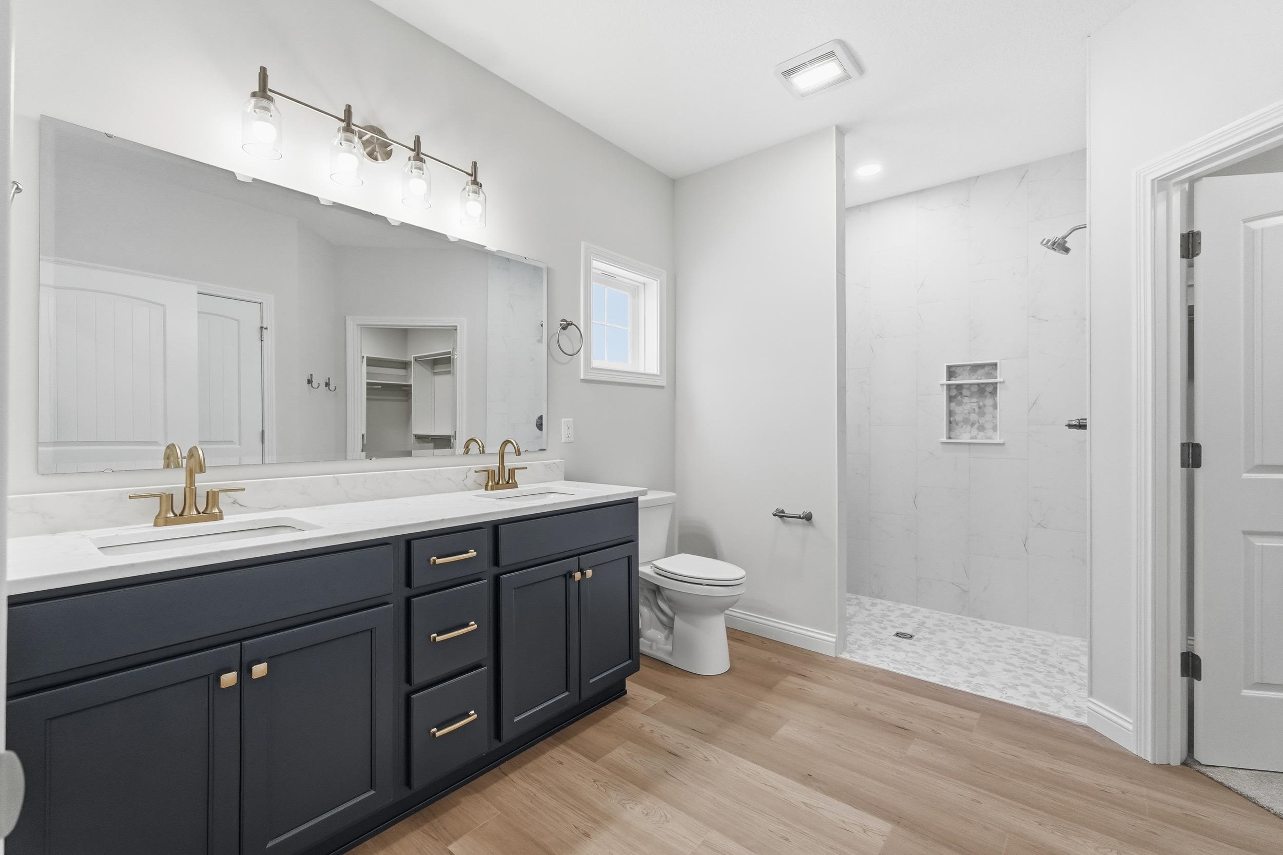 Bathroom with double vanity, tiled shower, light wood finished floors, and a spacious closet