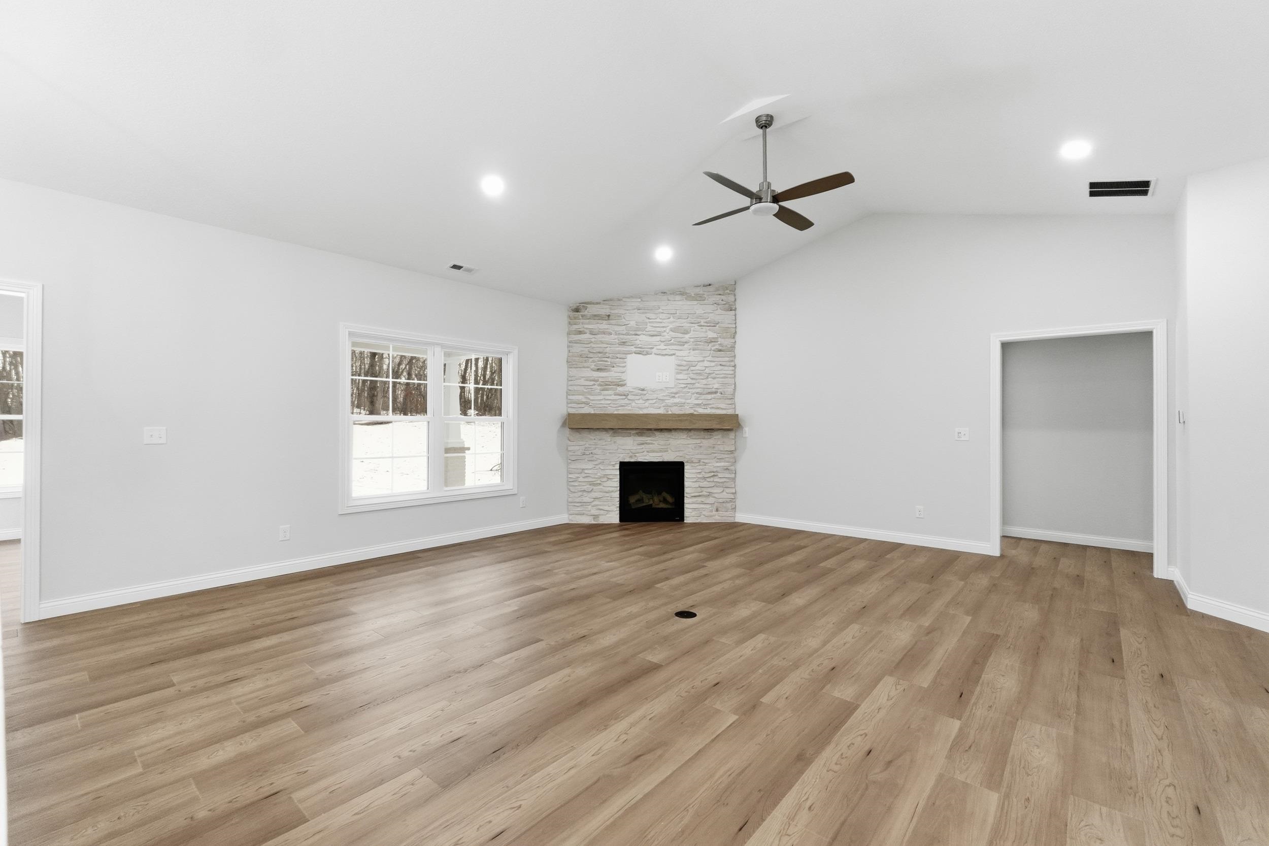 Unfurnished living room featuring light wood-type flooring, lofted ceiling, a stone fireplace, recessed lighting, and ceiling fan