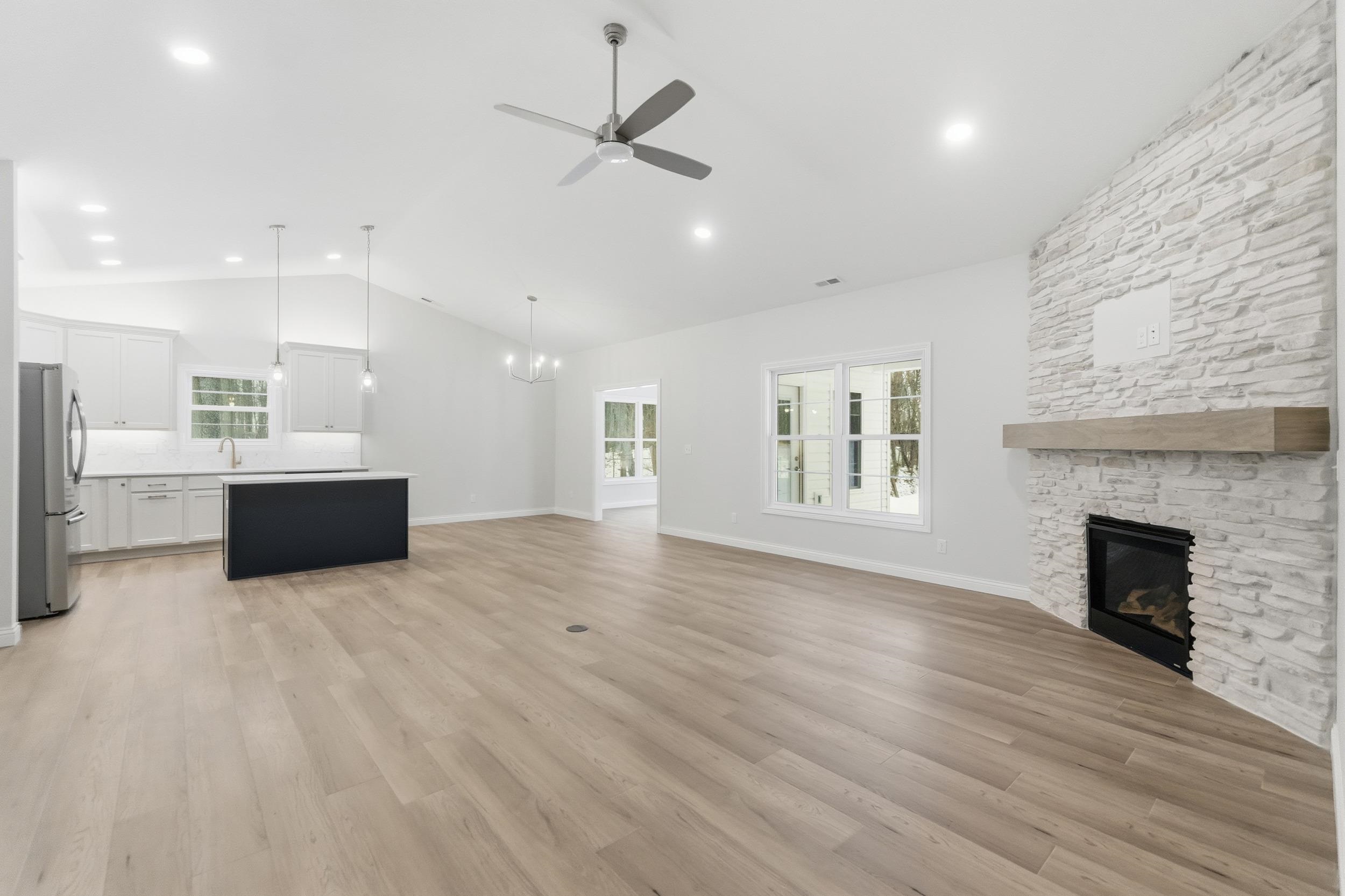Unfurnished living room featuring a fireplace, light wood finished floors, a ceiling fan, vaulted ceiling