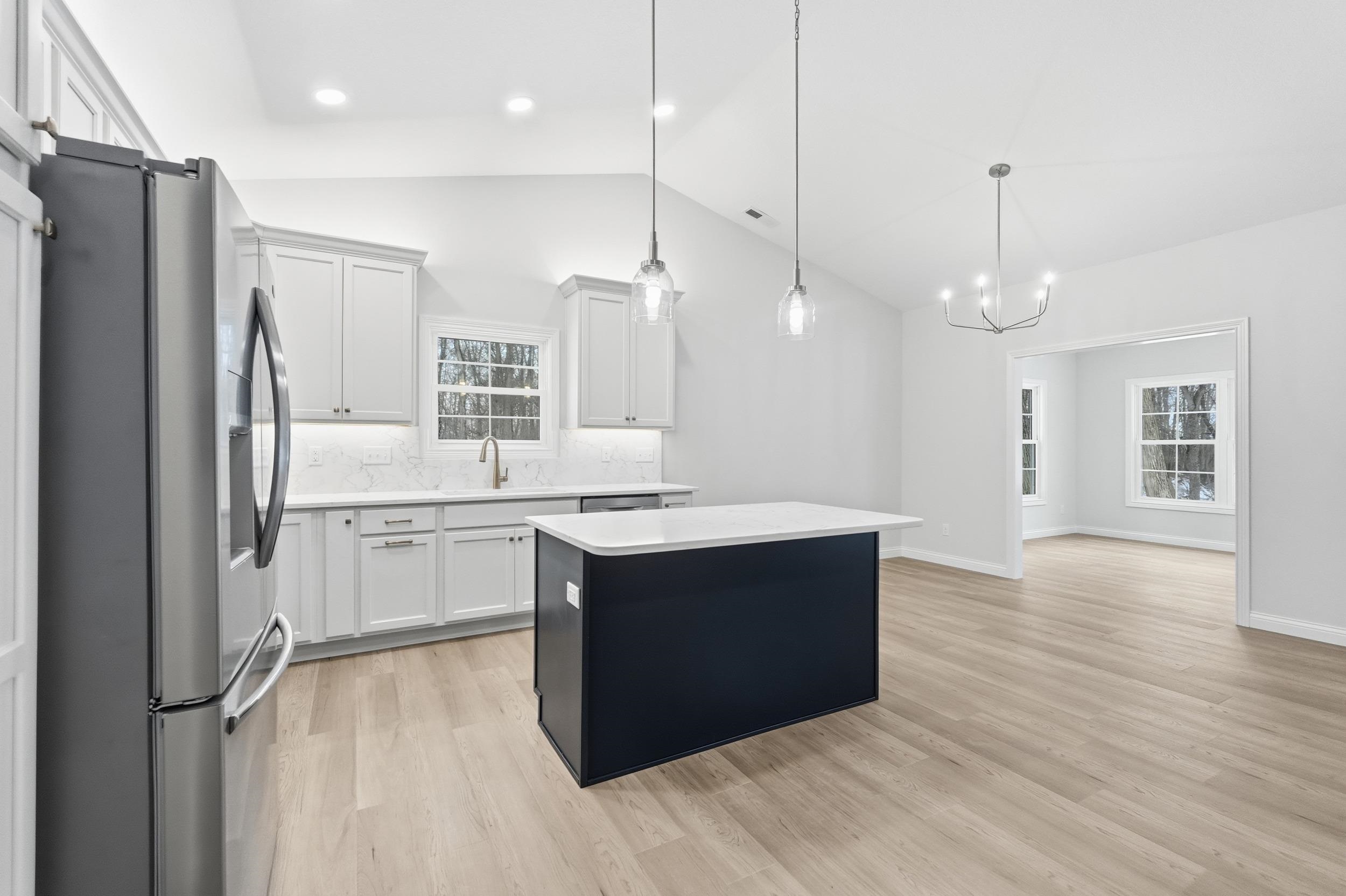 Kitchen featuring stainless steel fridge with ice dispenser, a center island, white cabinets, lofted ceiling, and hanging light fixtures