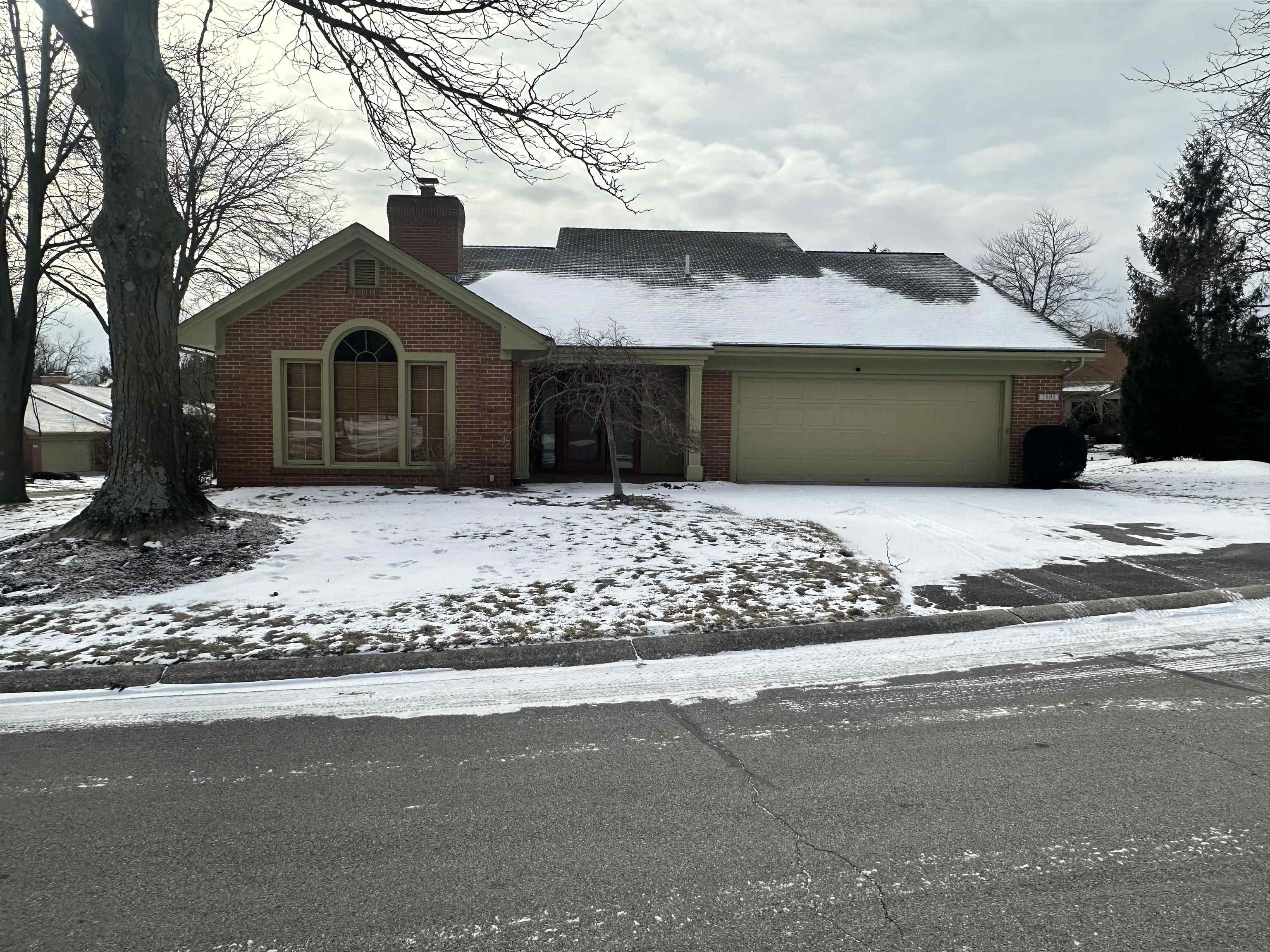 View of front of property featuring brick siding, an attached garage, a chimney, and driveway