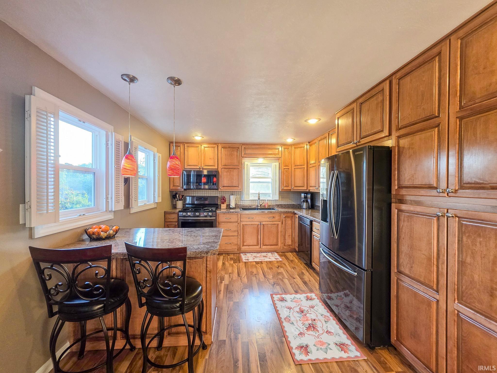Kitchen featuring a peninsula, a breakfast bar, stainless steel appliances, light wood-style floors, and pendant lighting