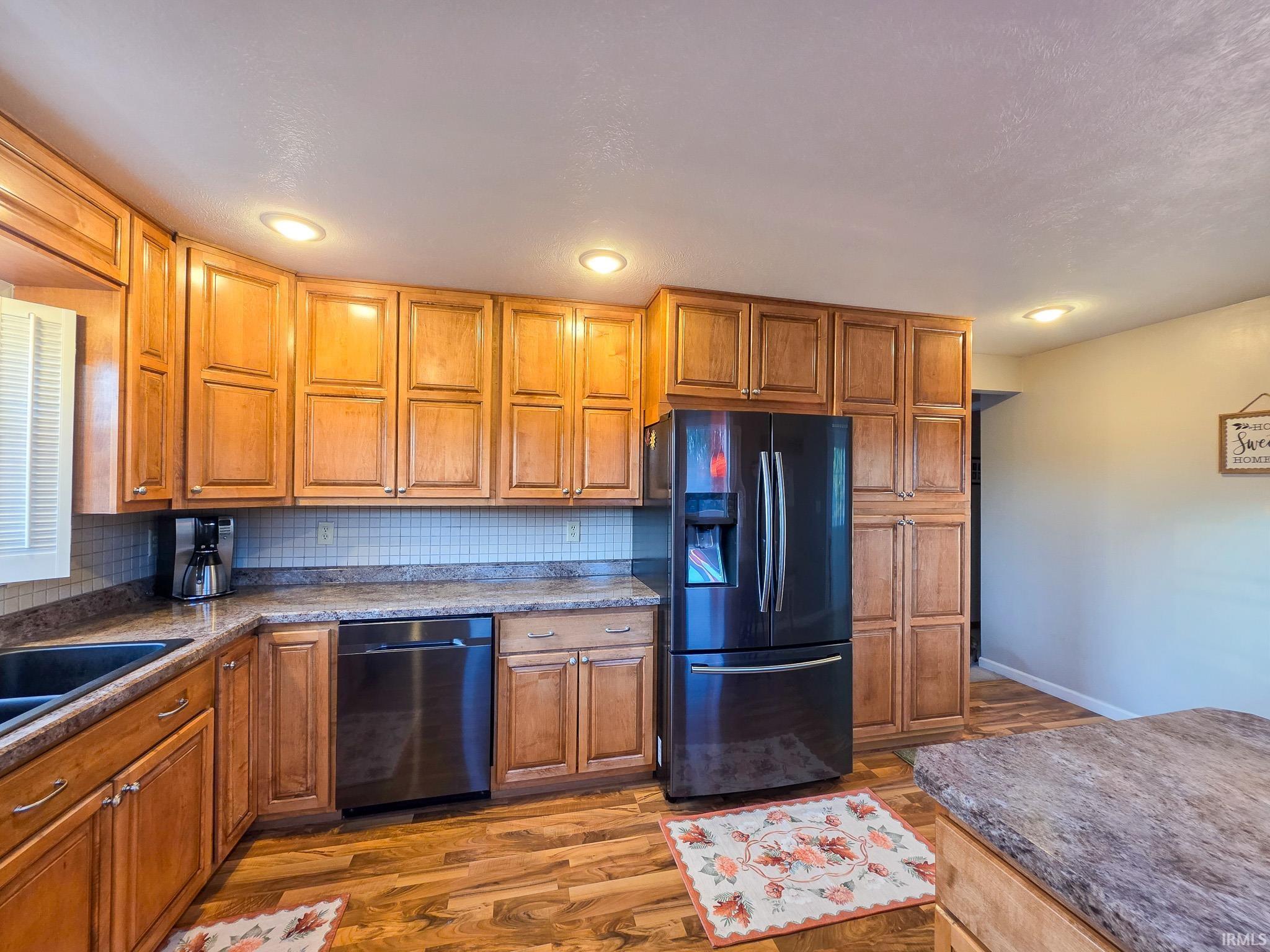 Kitchen with wood finish cabinets, black fridge, dishwasher, dark wood-style flooring, and recessed lighting