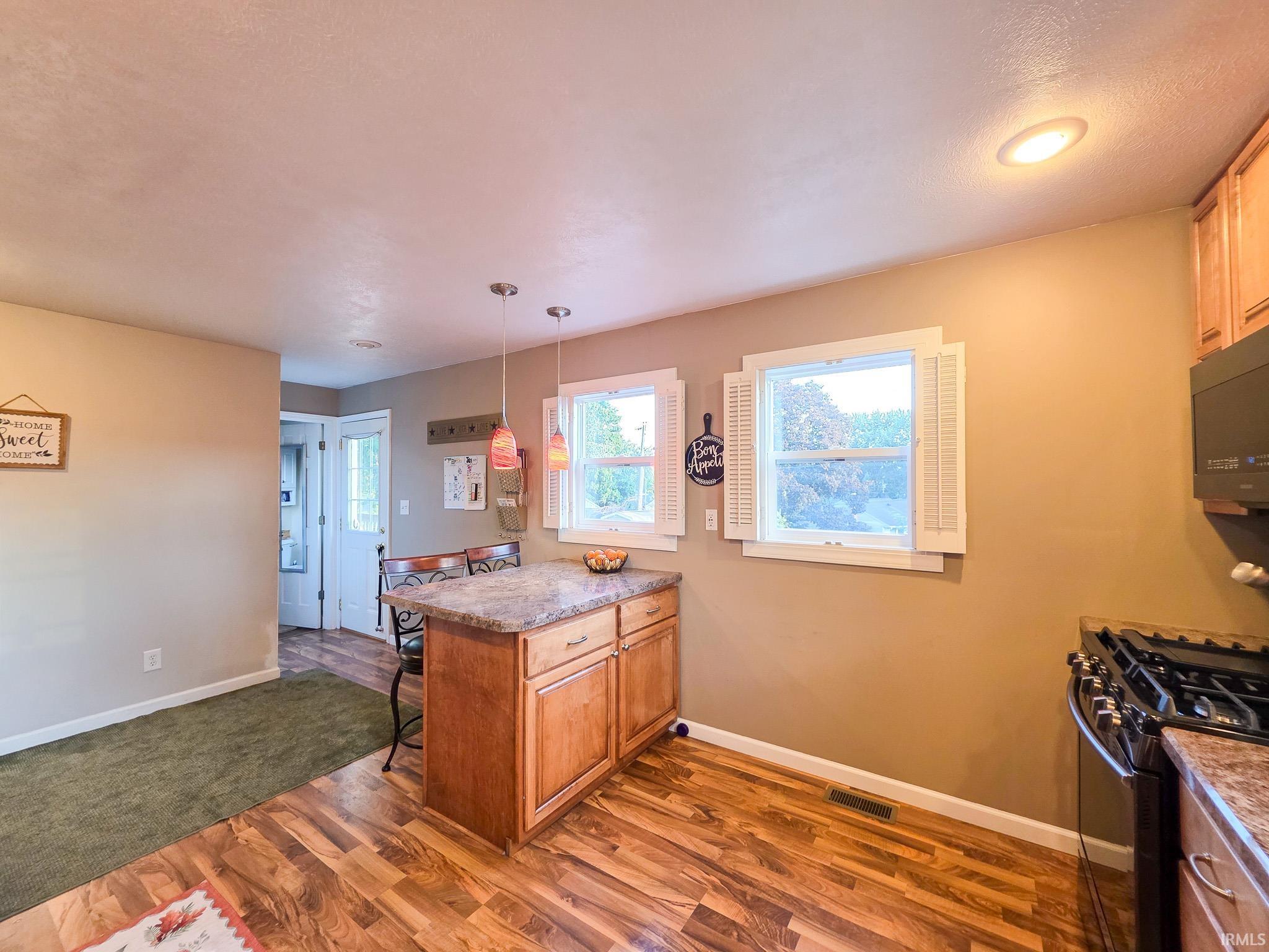 Kitchen with a peninsula, a kitchen bar, black range with gas cooktop, dark wood-type flooring, and pendant lighting