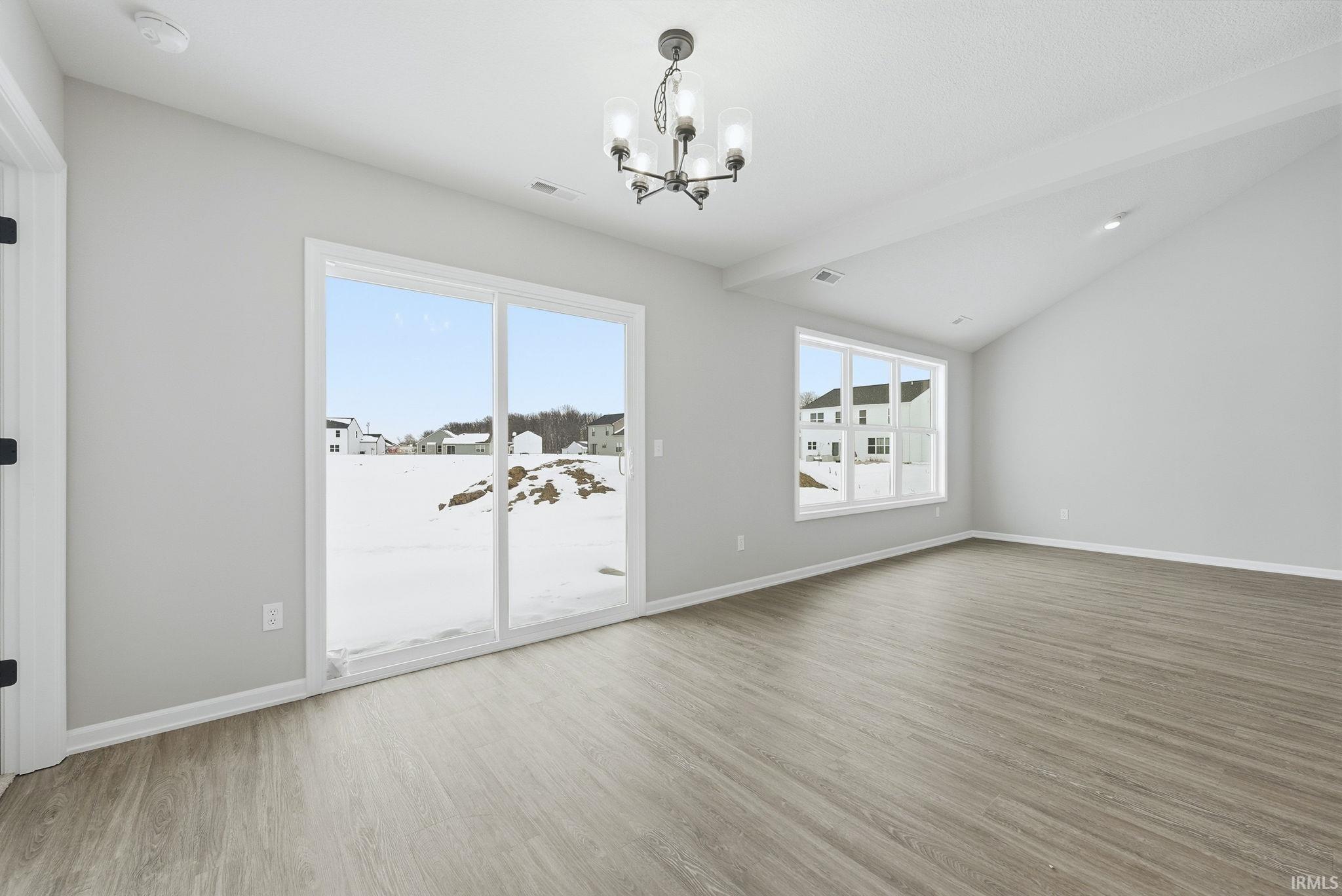 Unfurnished room featuring suspended lighting, light wood-style floors, and vaulted ceiling with beams