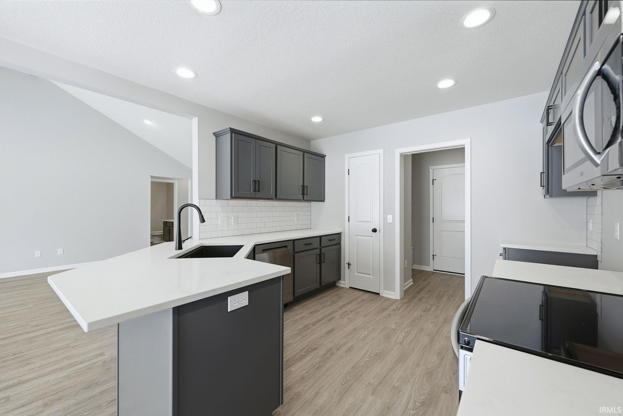 Kitchen featuring stainless steel appliances, a peninsula, light wood-type flooring, gray cabinets, and backsplash
