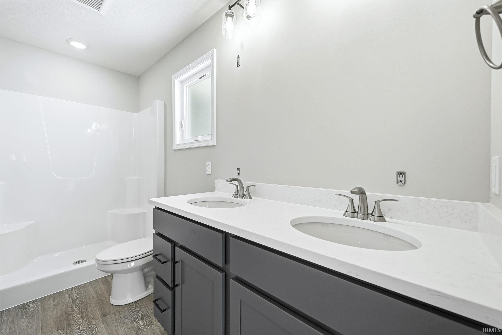 Full bathroom featuring double vanity, a shower stall, and dark wood finished floors