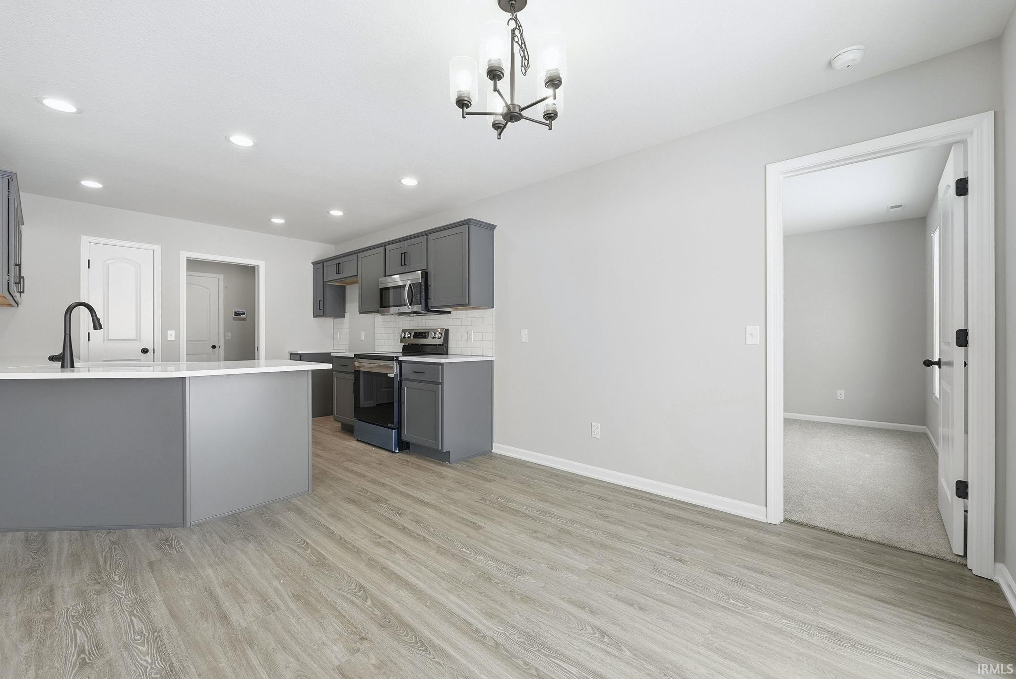 Kitchen with stainless steel appliances, a peninsula, gray cabinets, tasteful backsplash, and light stone countertops