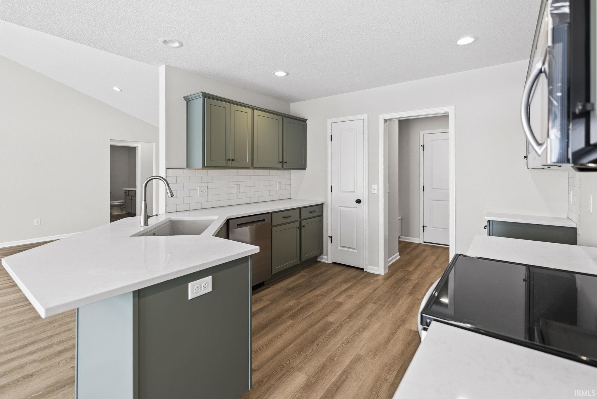 Kitchen with a peninsula, stainless steel dishwasher, light stone countertops, dark wood finished floors, and decorative backsplash