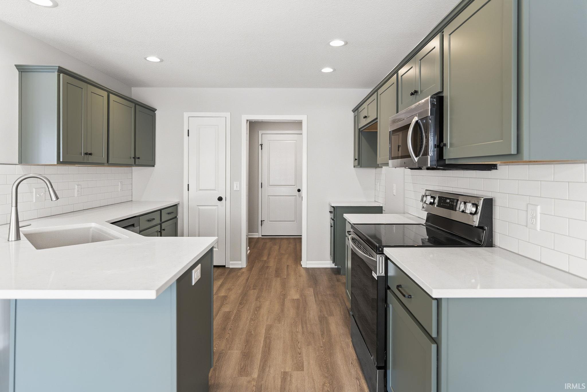 Kitchen with decorative backsplash, stainless steel appliances, a peninsula, light stone counters, and recessed lighting