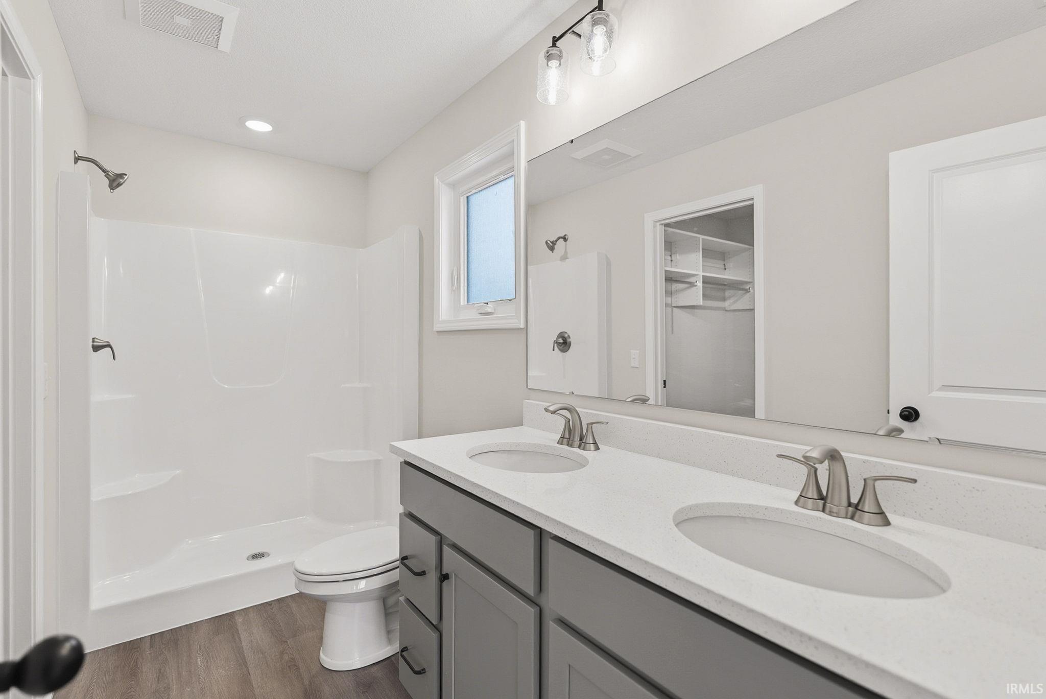 Bathroom featuring a shower stall, double vanity, dark wood-style floors, a walk in closet, and recessed lighting