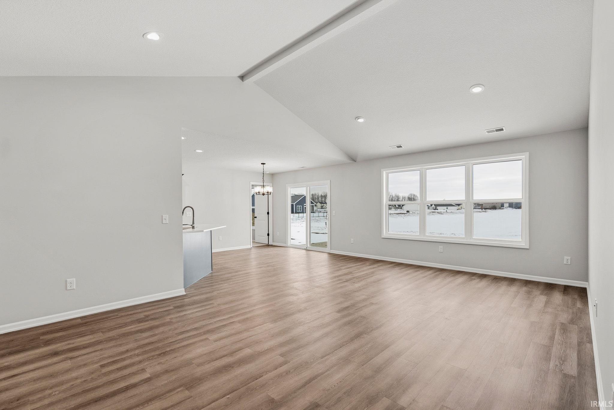 Unfurnished living room with beamed ceiling, light wood-type flooring, and a chandelier