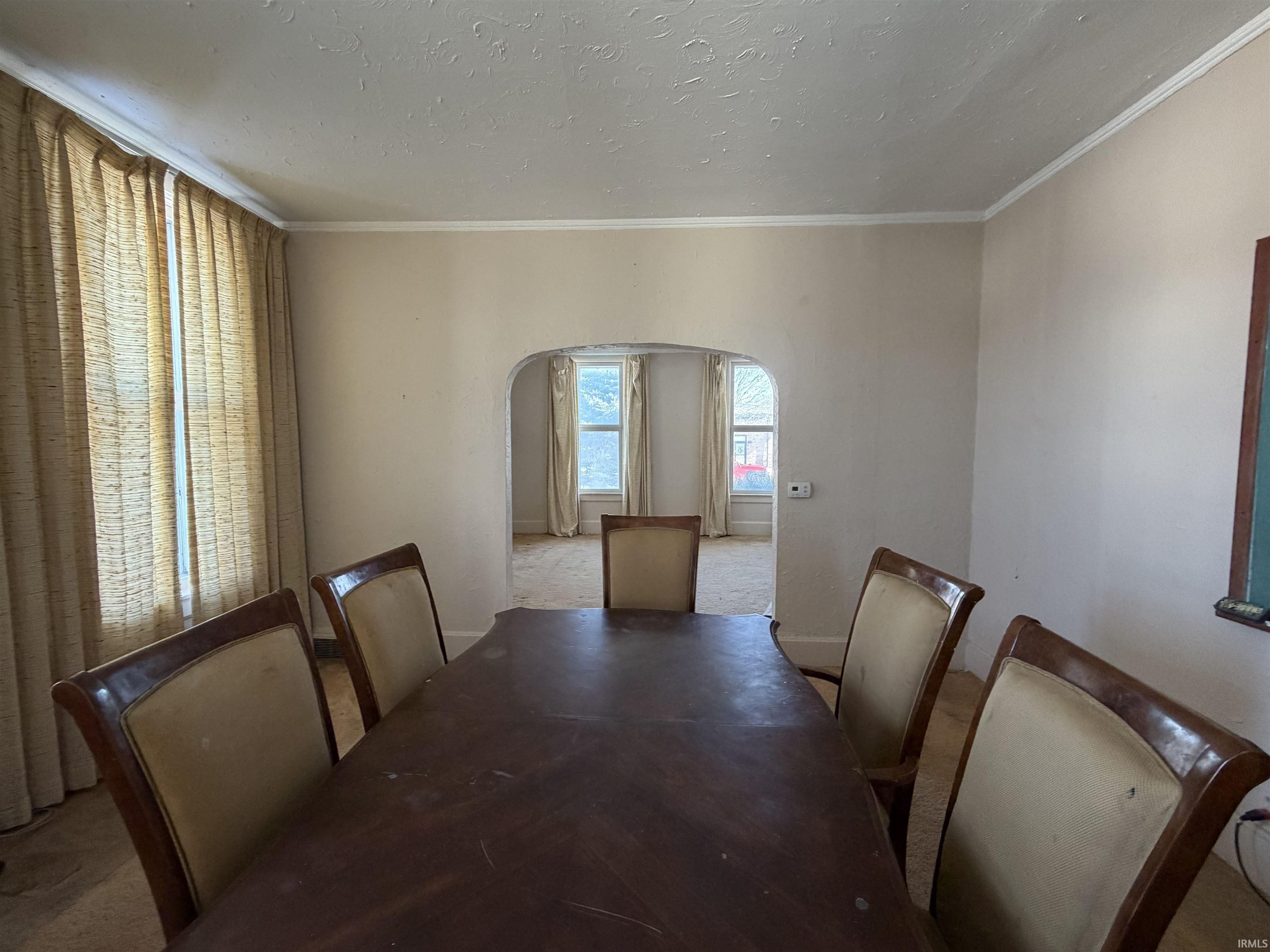 Unfurnished dining area featuring carpet flooring, arched walkways, a textured ceiling, and crown molding