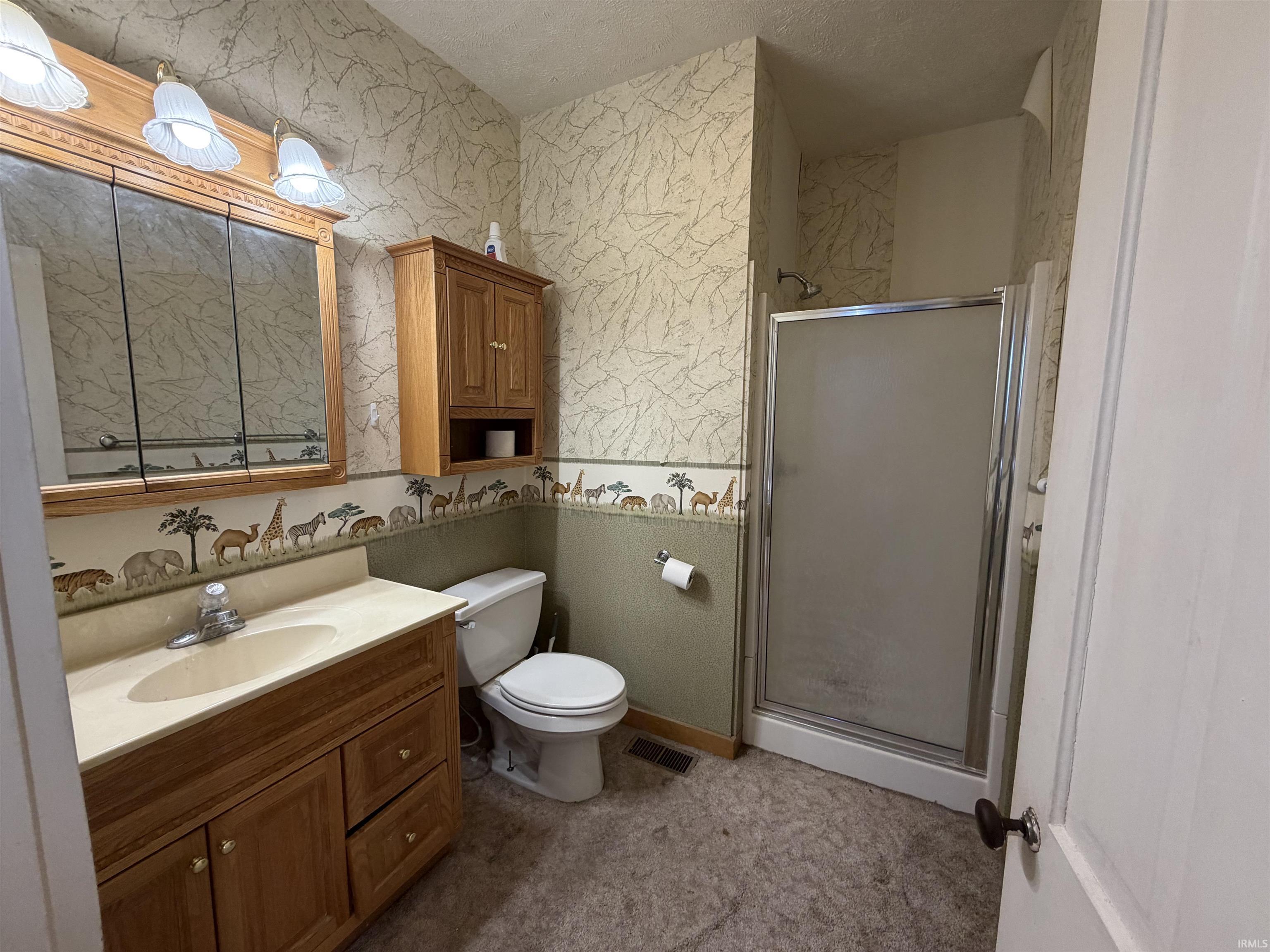 Full bathroom featuring vanity, a shower stall, a textured ceiling, and wallpapered walls