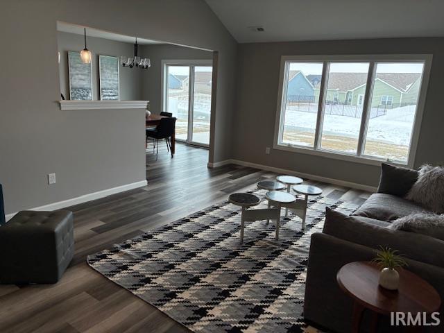 Living area featuring dark wood-style floors, vaulted ceiling, and a chandelier
