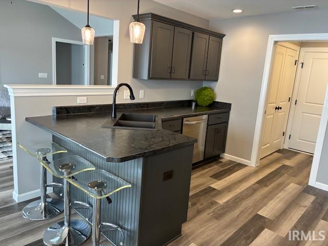 Kitchen with a breakfast bar area, a peninsula, hanging light fixtures, dark countertops, and dark wood-style floors