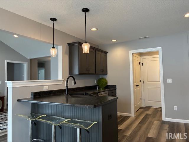Kitchen featuring dark countertops, decorative light fixtures, a kitchen breakfast bar, a peninsula, and dark wood finished floors