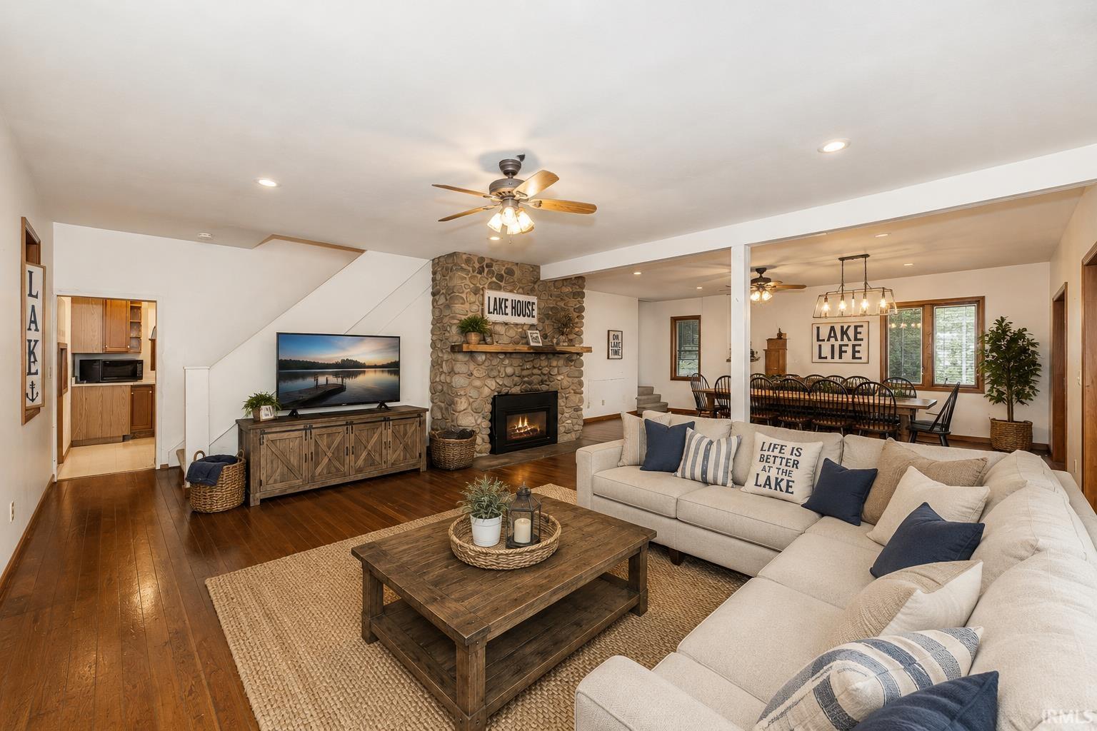 Spacious living area featuring rich wood-finish flooring, a stone fireplace with a built-in mantel, and recessed lighting
