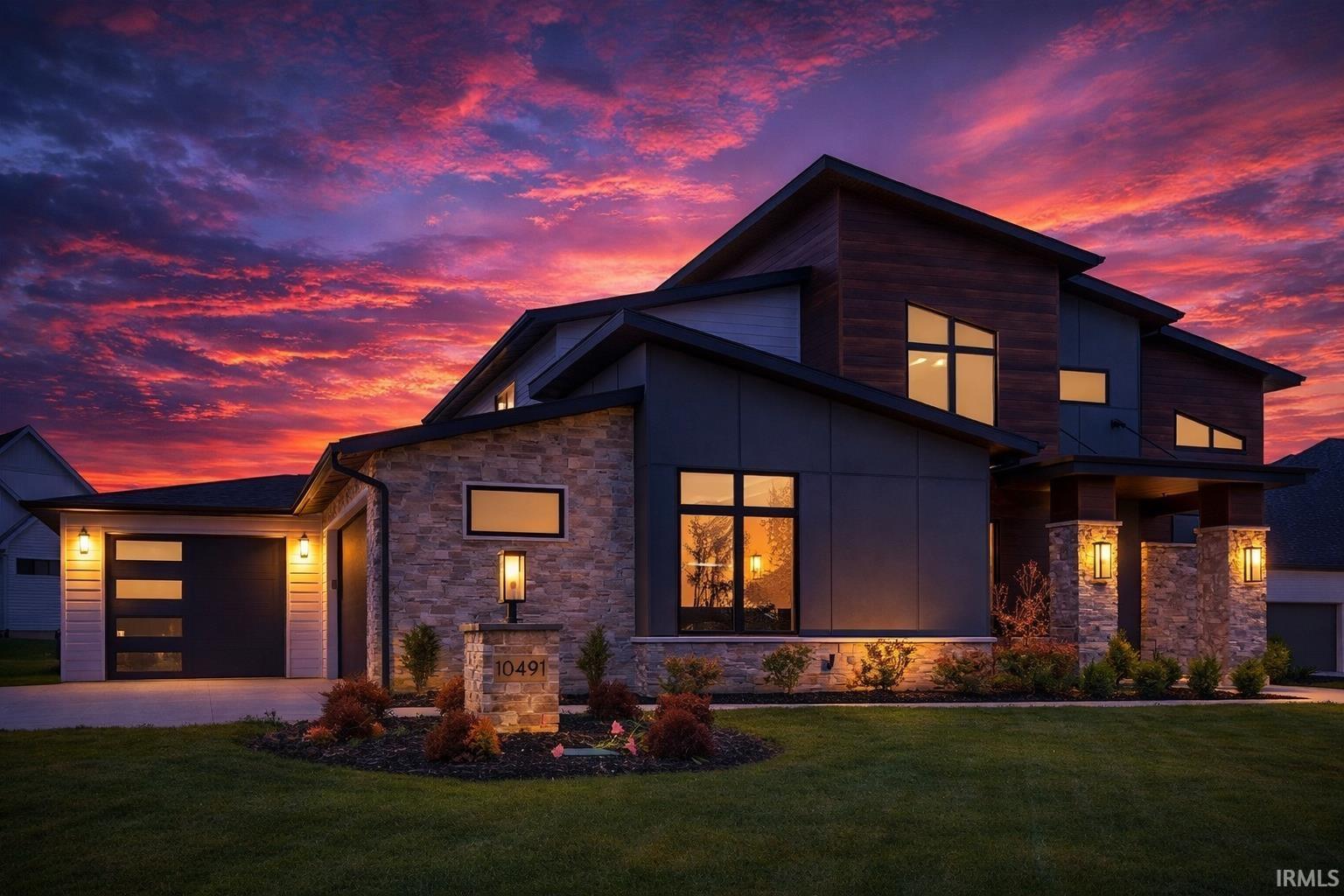 Contemporary home featuring stone siding, a yard, a garage, and driveway