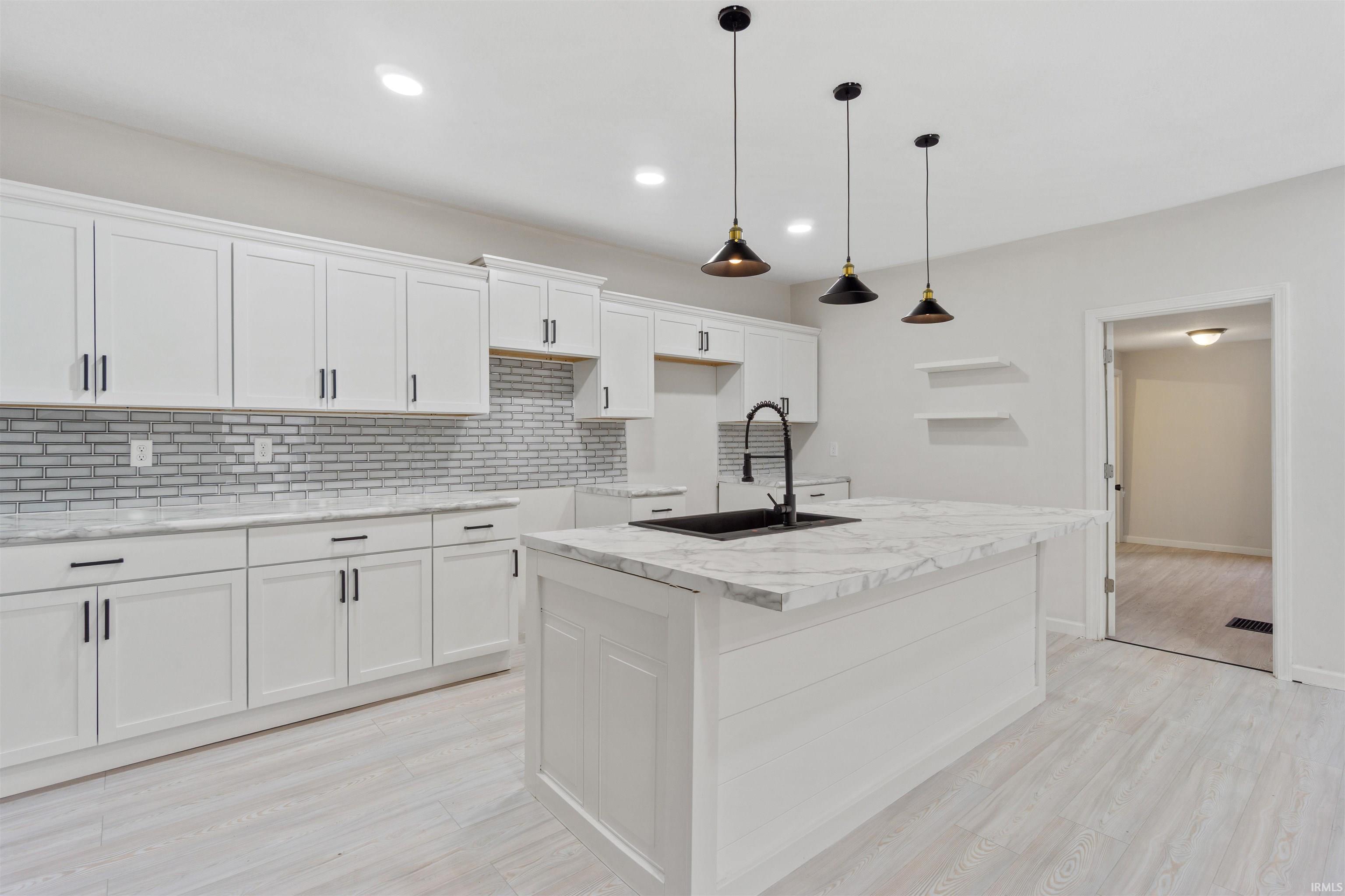 Kitchen with decorative backsplash, white cabinetry, decorative light fixtures, an island with sink, and light wood-style floors