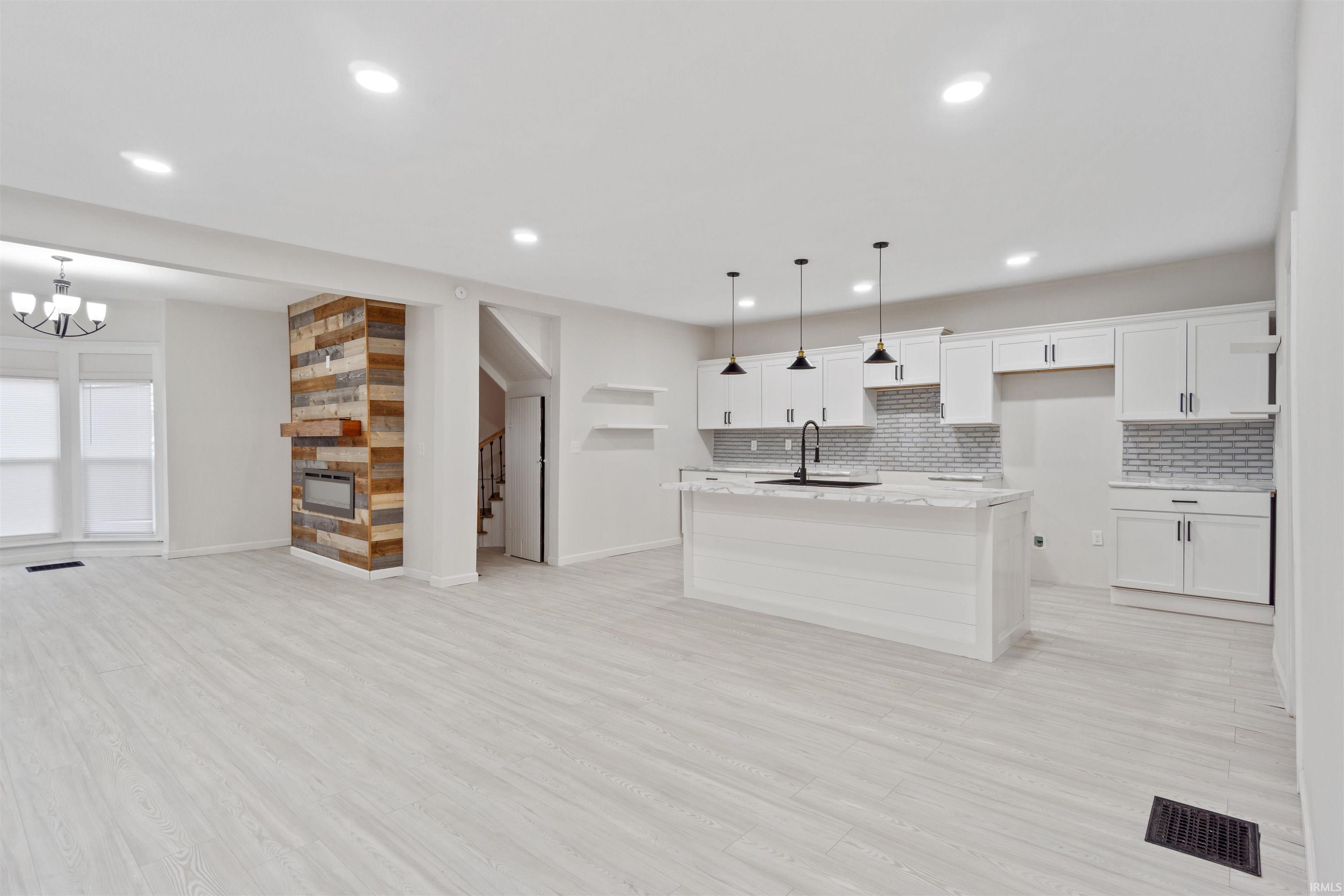 Kitchen with white cabinets, pendant lighting, a center island with sink, decorative backsplash, and open shelves