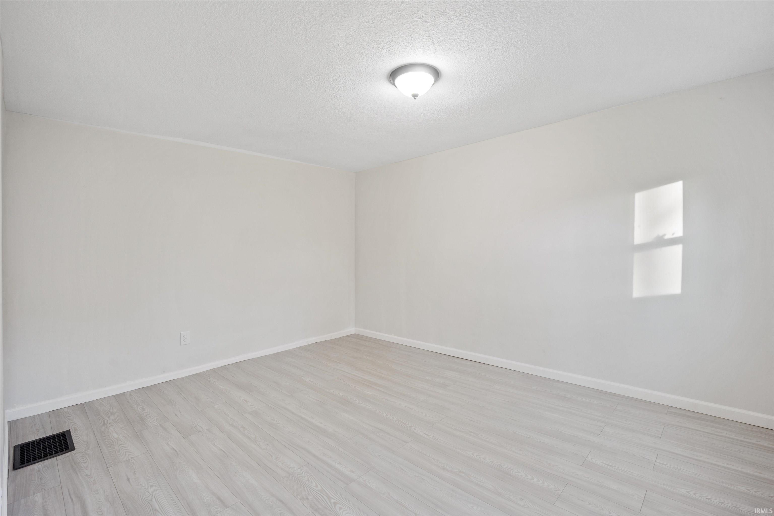 Unfurnished room with light wood-type flooring and a textured ceiling